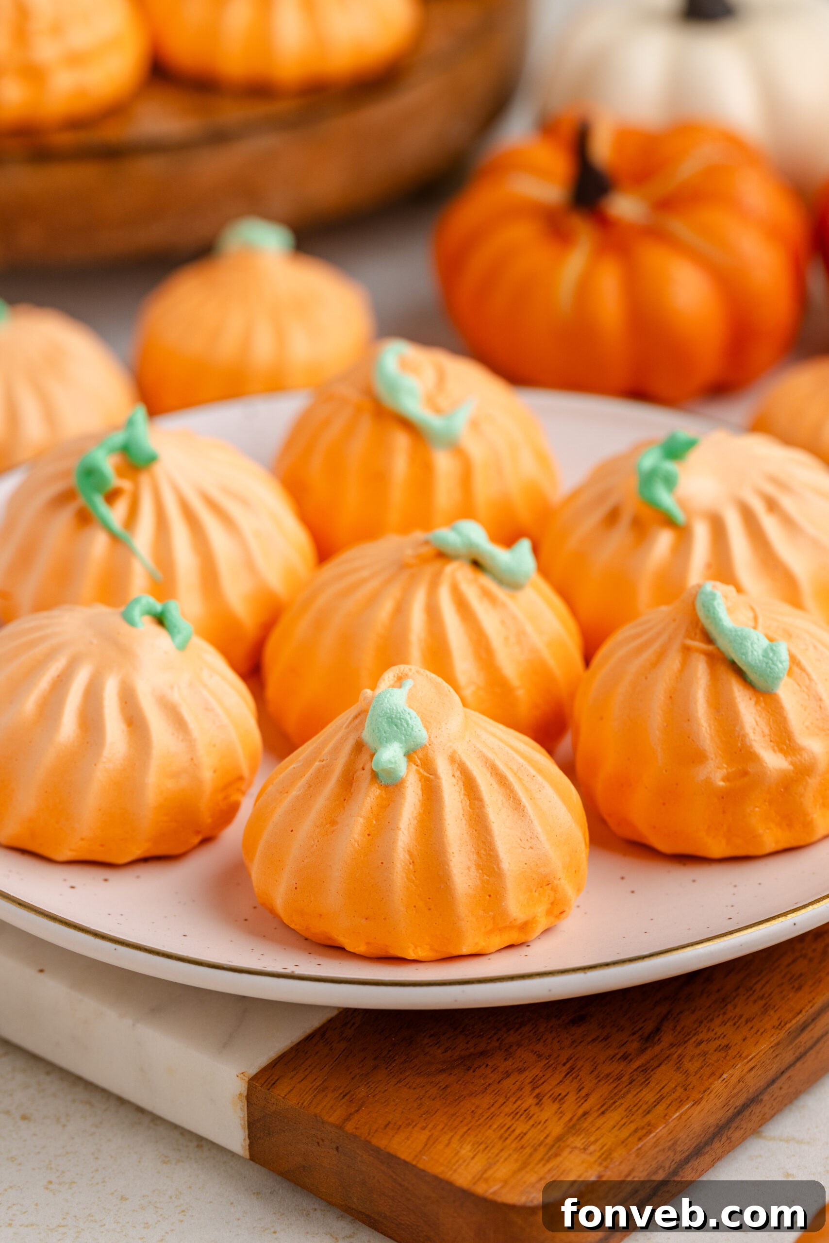 Pumpkin Meringue cookies on a plate with faux pumpkins behind it on table and a tray with more cookies 