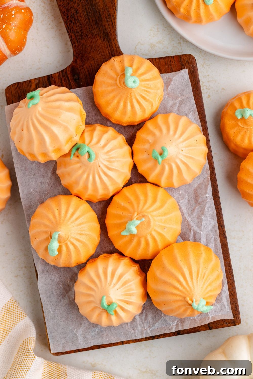 Crisp meringue cookies that look like pumpkins on a wooden tray and more on plates and placed on white table to give a fall themed look 