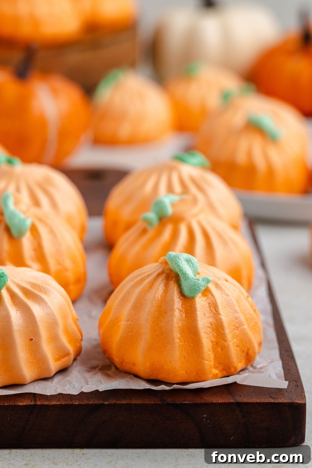 side view of table with a wooden tray with Pumpkin Meringues placed in single rows and more cookies behind it on table 