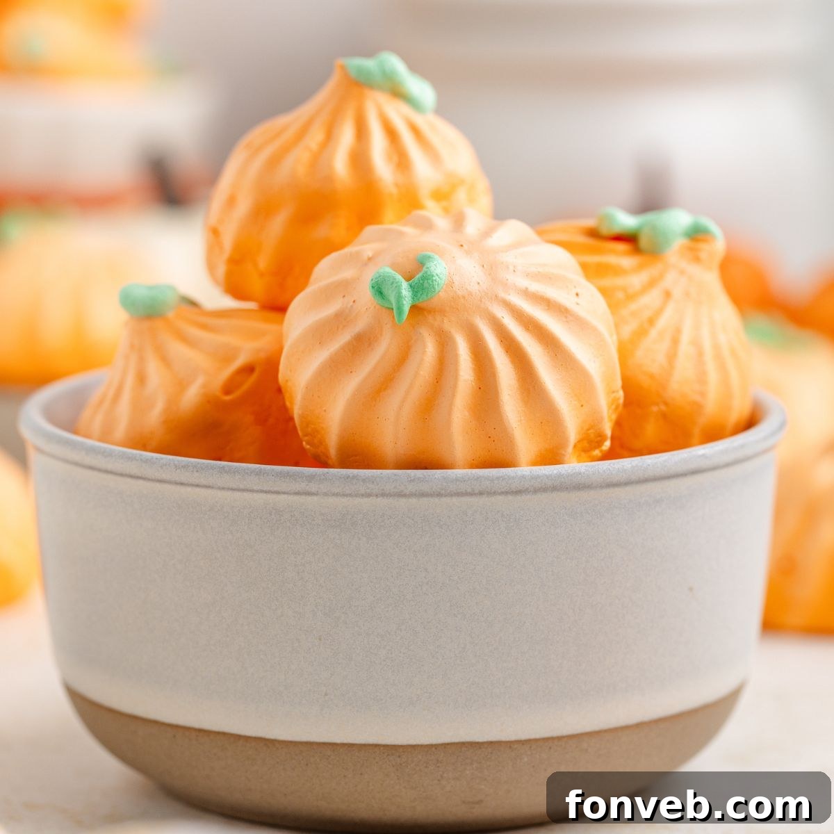 Pumpkin Meringues placed in a white bowl on table with more meringues behind it on table 