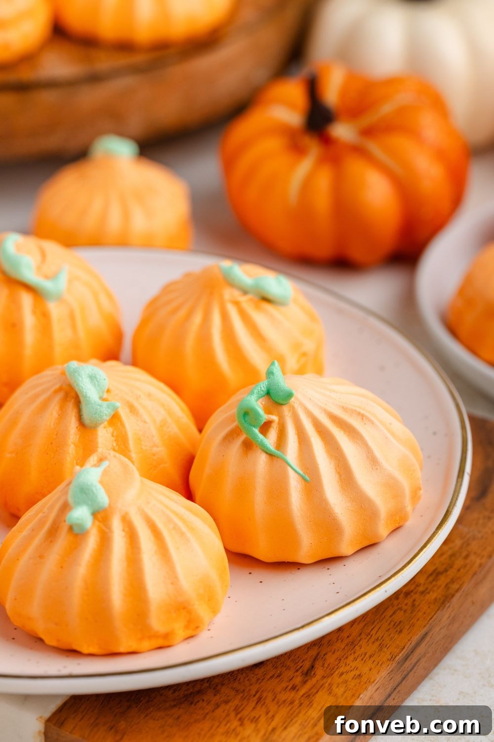 Pumpkin Meringue cookies on a plate with faux pumpkins behind it on table and a tray with more cookies 