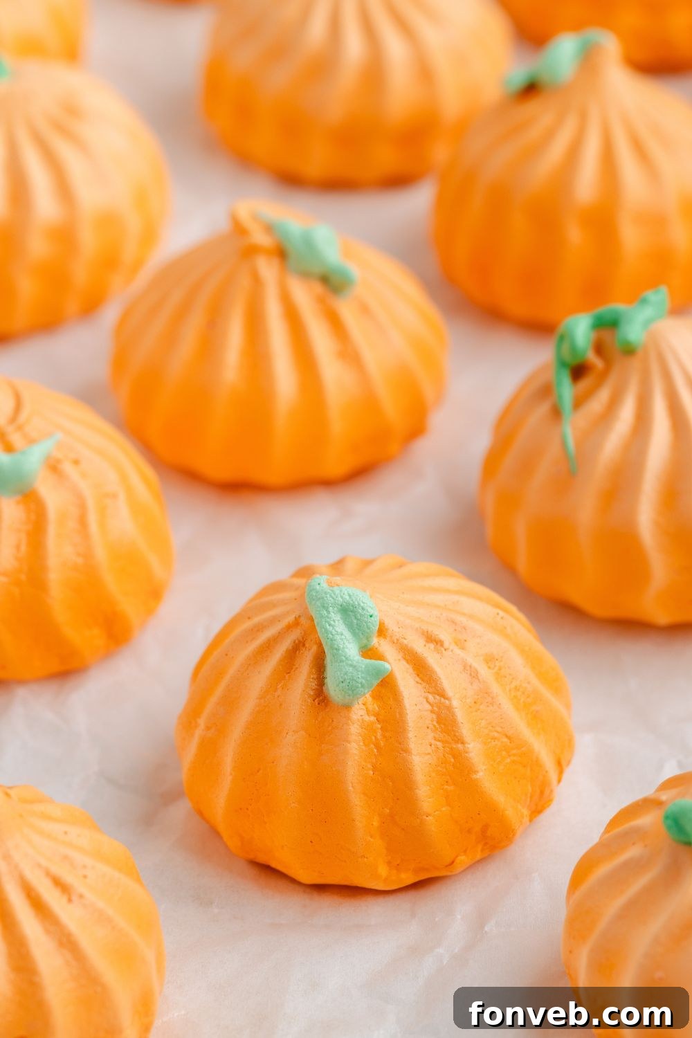 Whipped egg white cookies that look like pumpkins in a single row sitting on white table