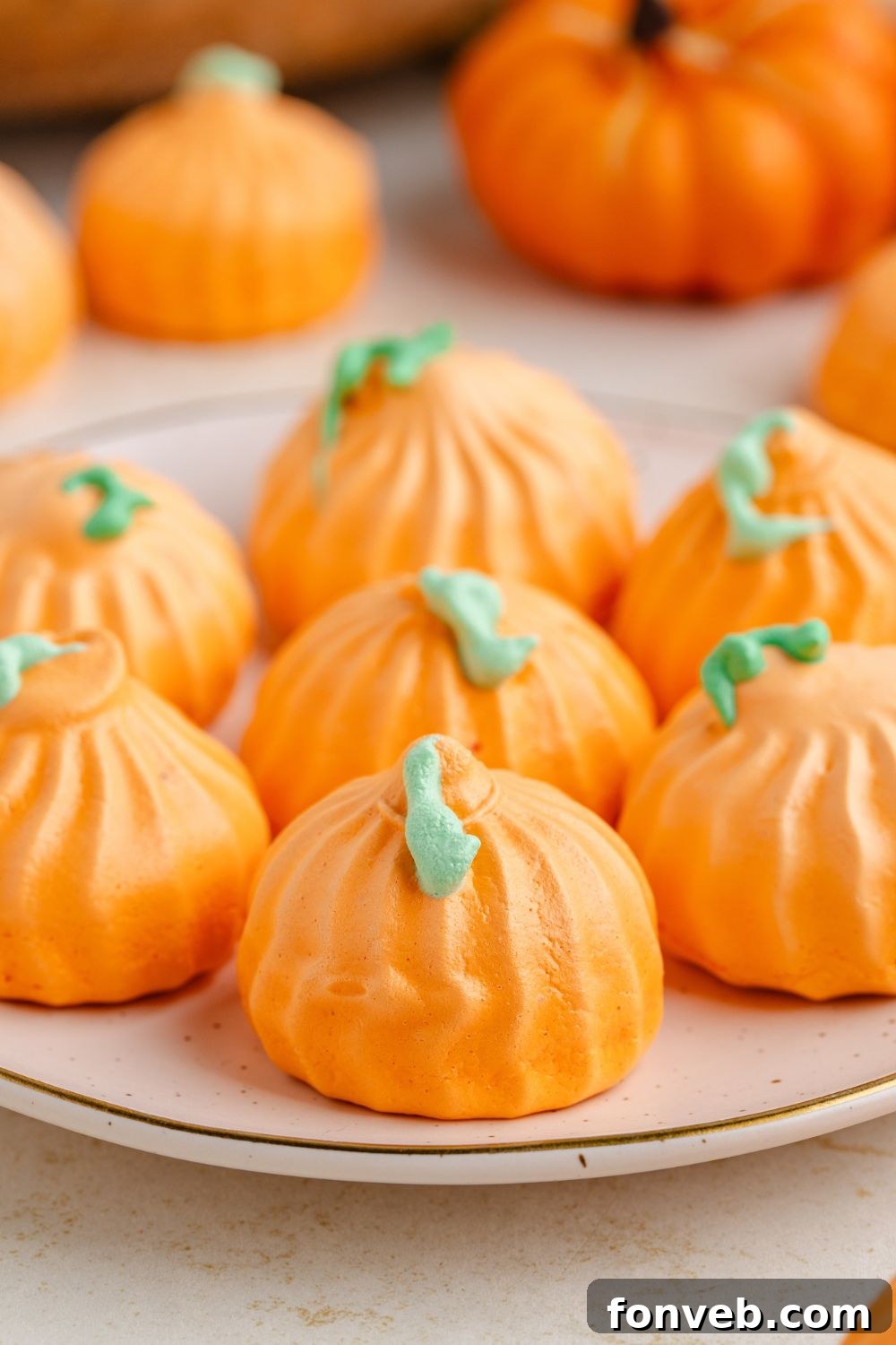 Pumpkin Meringues on a white plate sitting on counter with a few more meringue cookies behind it 