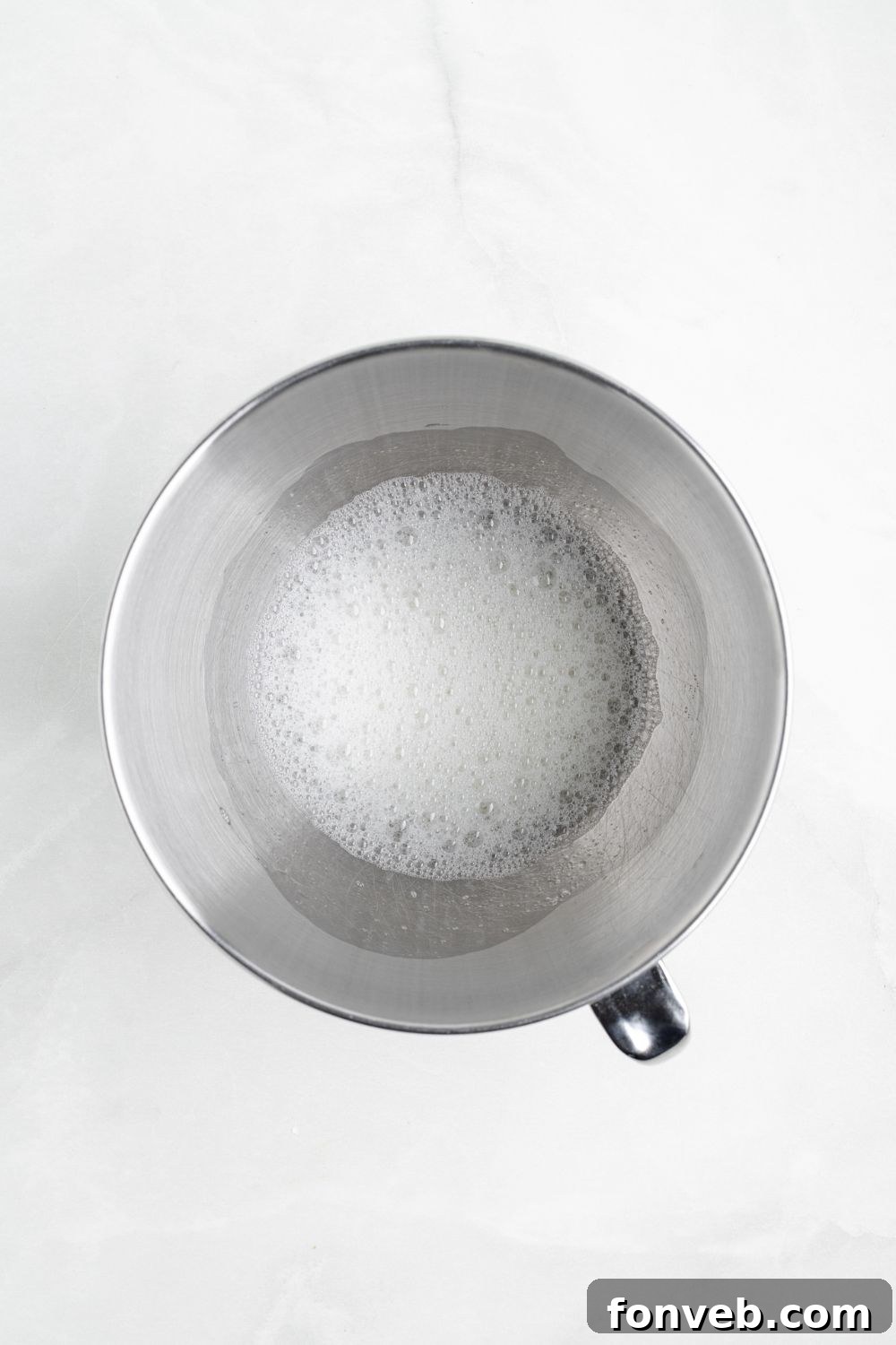 egg whites in a metal mixing bowl on a white counter 