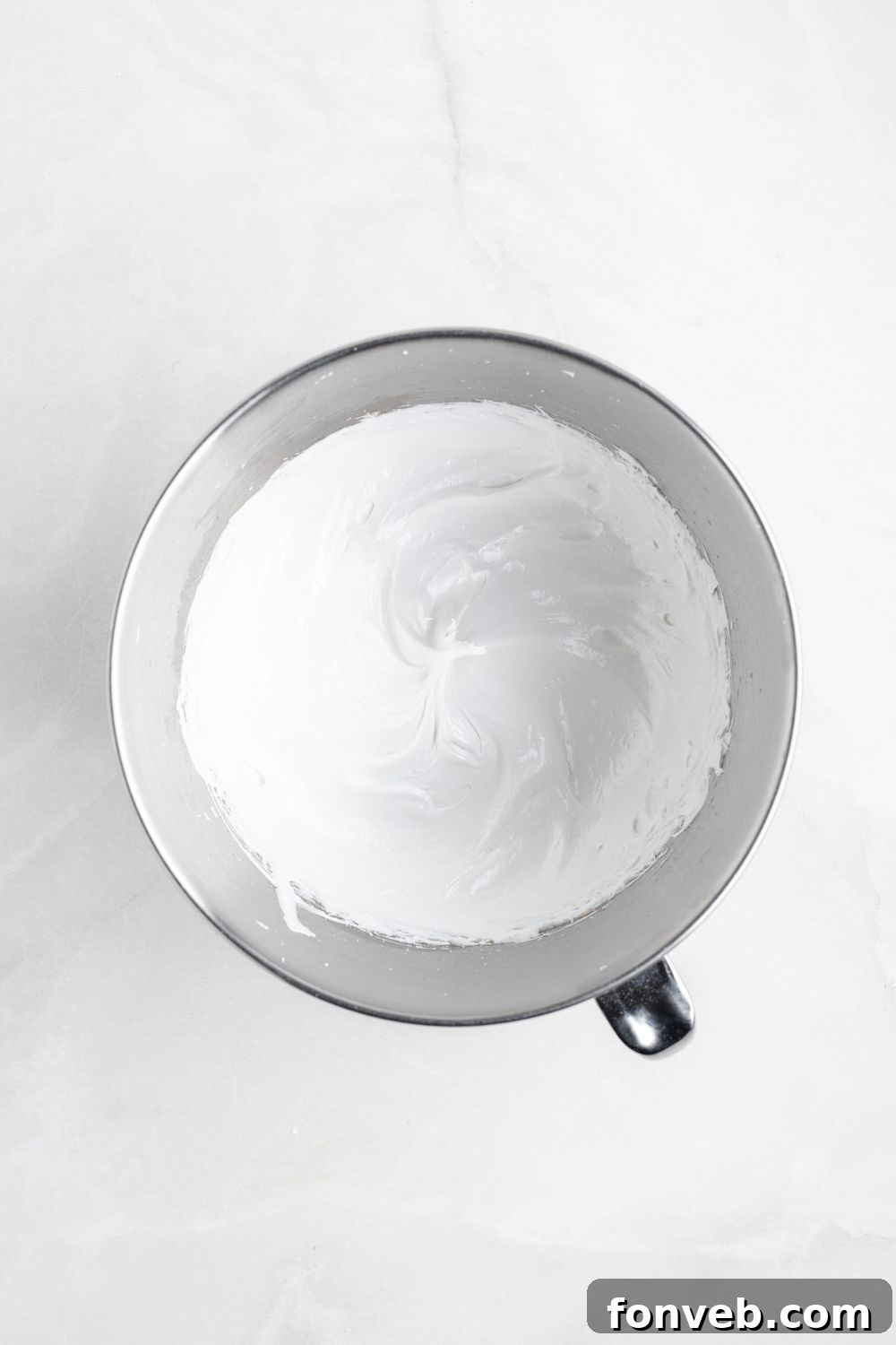 fluffy whipped meringue in a metal mixing bowl on a white counter