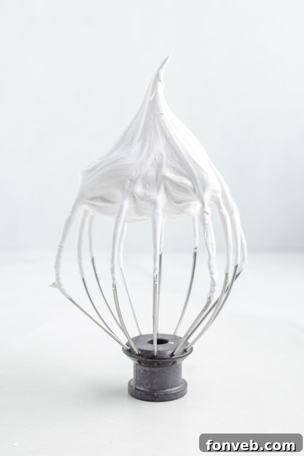 a whisk sitting on table with stiff meringue on it 