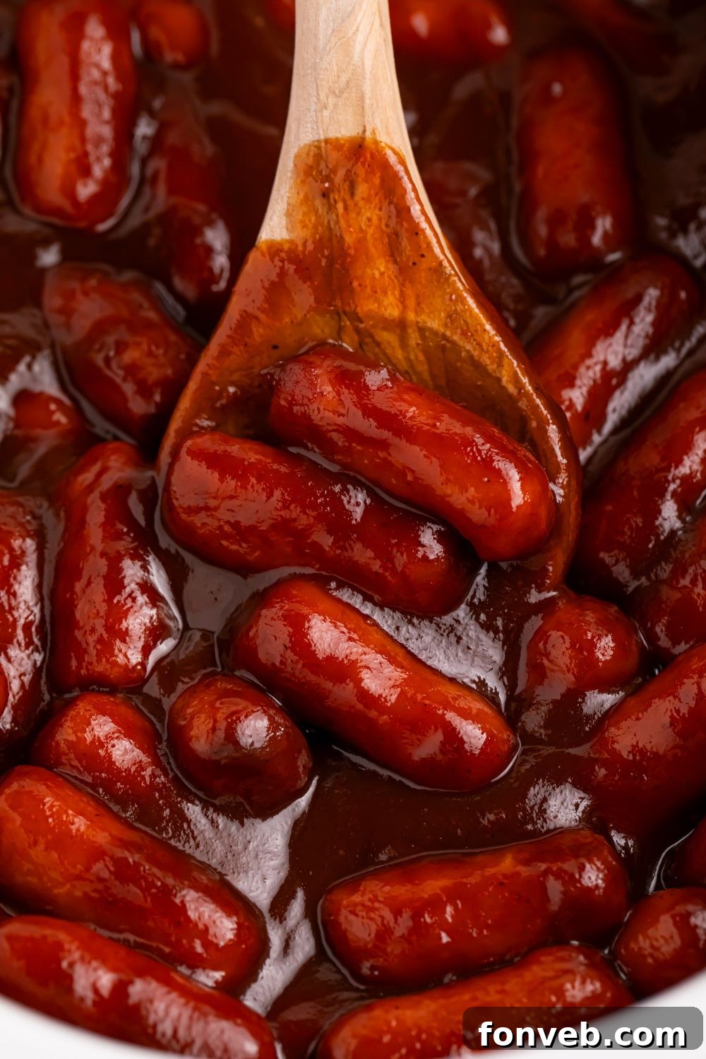 Sweet and Tangy Crockpot Apple Butter Smokies 11 looking down on a slow cooker full of lil smokies in an apple butter and bbq sauce mixture with a wooden spoon scooping some up