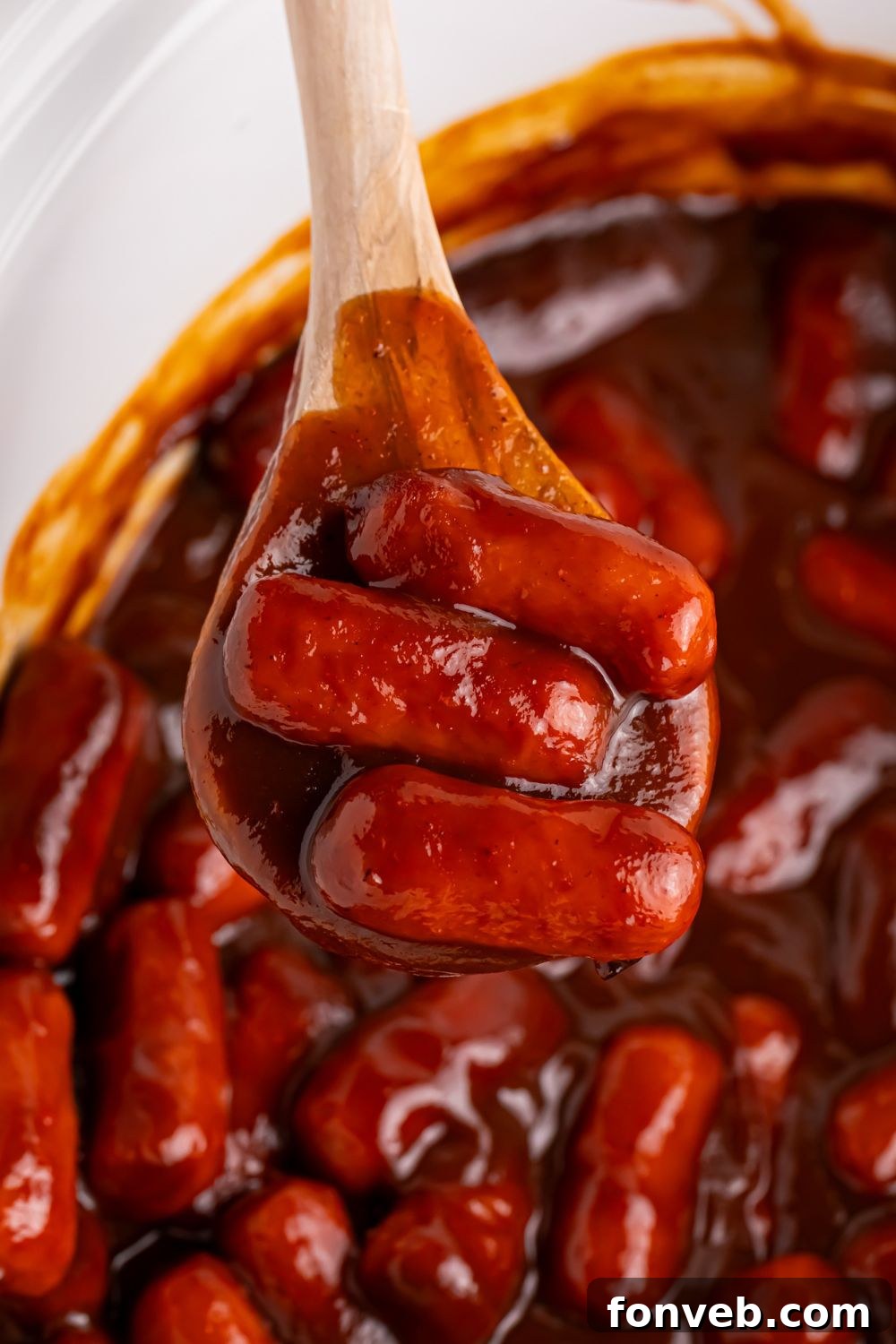 Sweet and Tangy Crockpot Apple Butter Smokies 12 Crockpot full of little smokies with apple butter and a wooden spoon scooping some of the lil smokies out of the crockpot