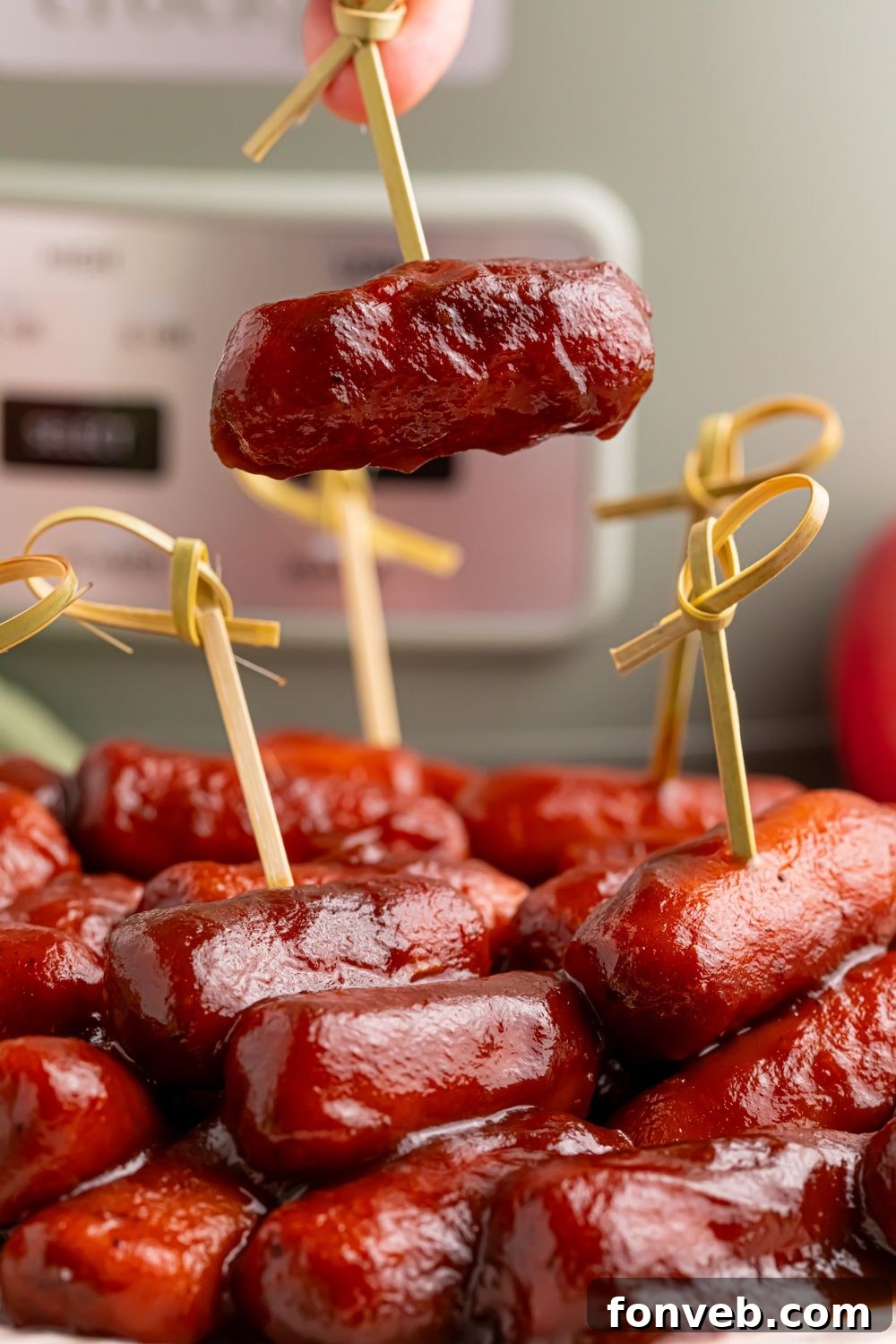 Sweet and Tangy Crockpot Apple Butter Smokies 15 toothpicks in smokies on a white platter with a crockpot sitting behind it