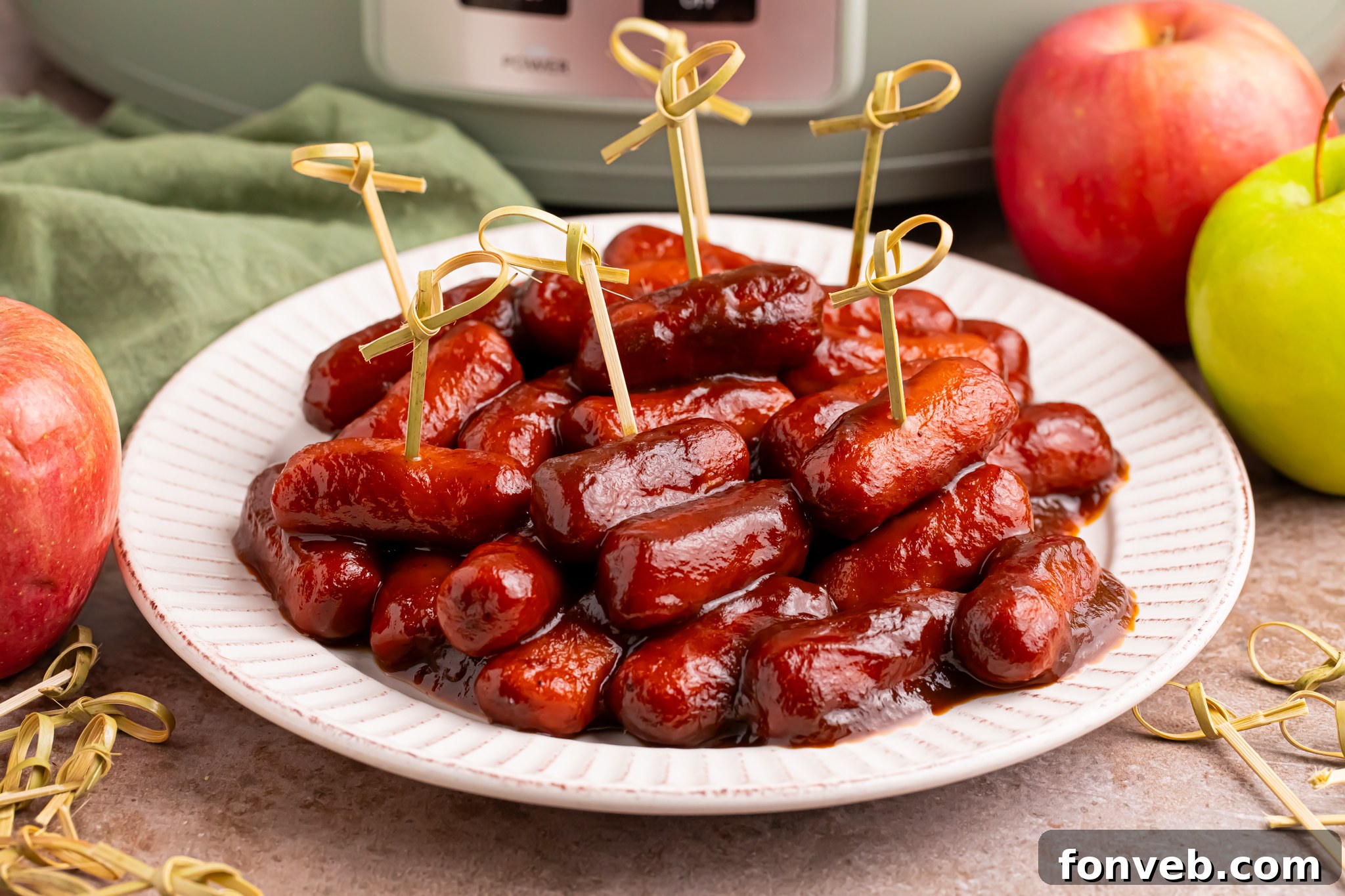 Sweet and Tangy Crockpot Apple Butter Smokies 17 toothpicks in smokies on a white platter with a crockpot sitting behind it