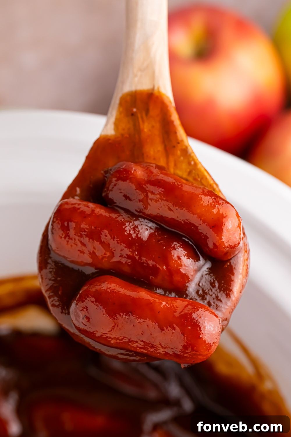 Sweet and Tangy Crockpot Apple Butter Smokies 3 wooden spoon with some Crockpot Apple Butter BBQ Little Smokies on it with apples behind it on the table