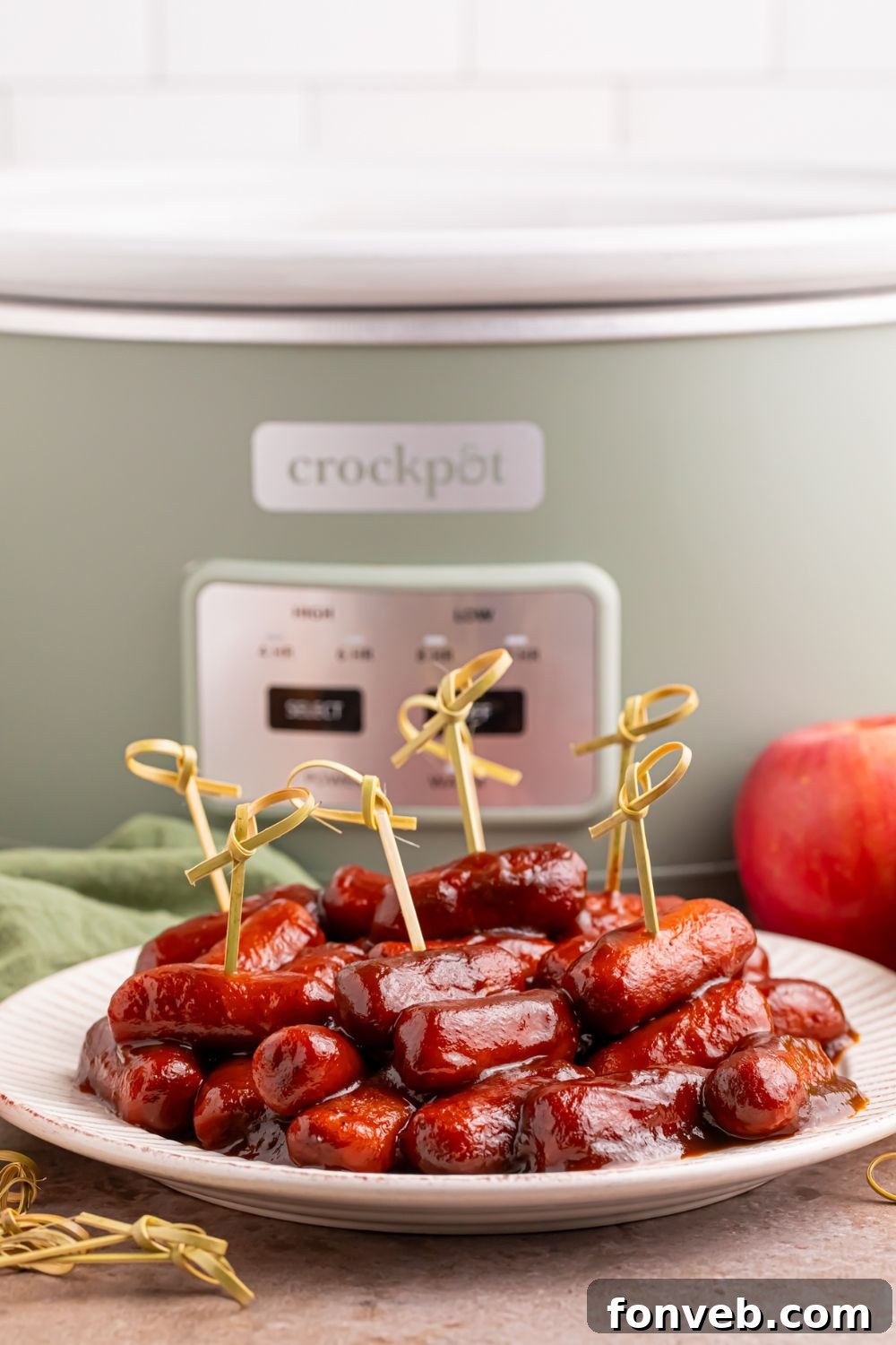 Sweet and Tangy Crockpot Apple Butter Smokies 9 crockpot on the table and in front of it you have a white plate full of bbq smokies with toothpicks for serving as an appetizer