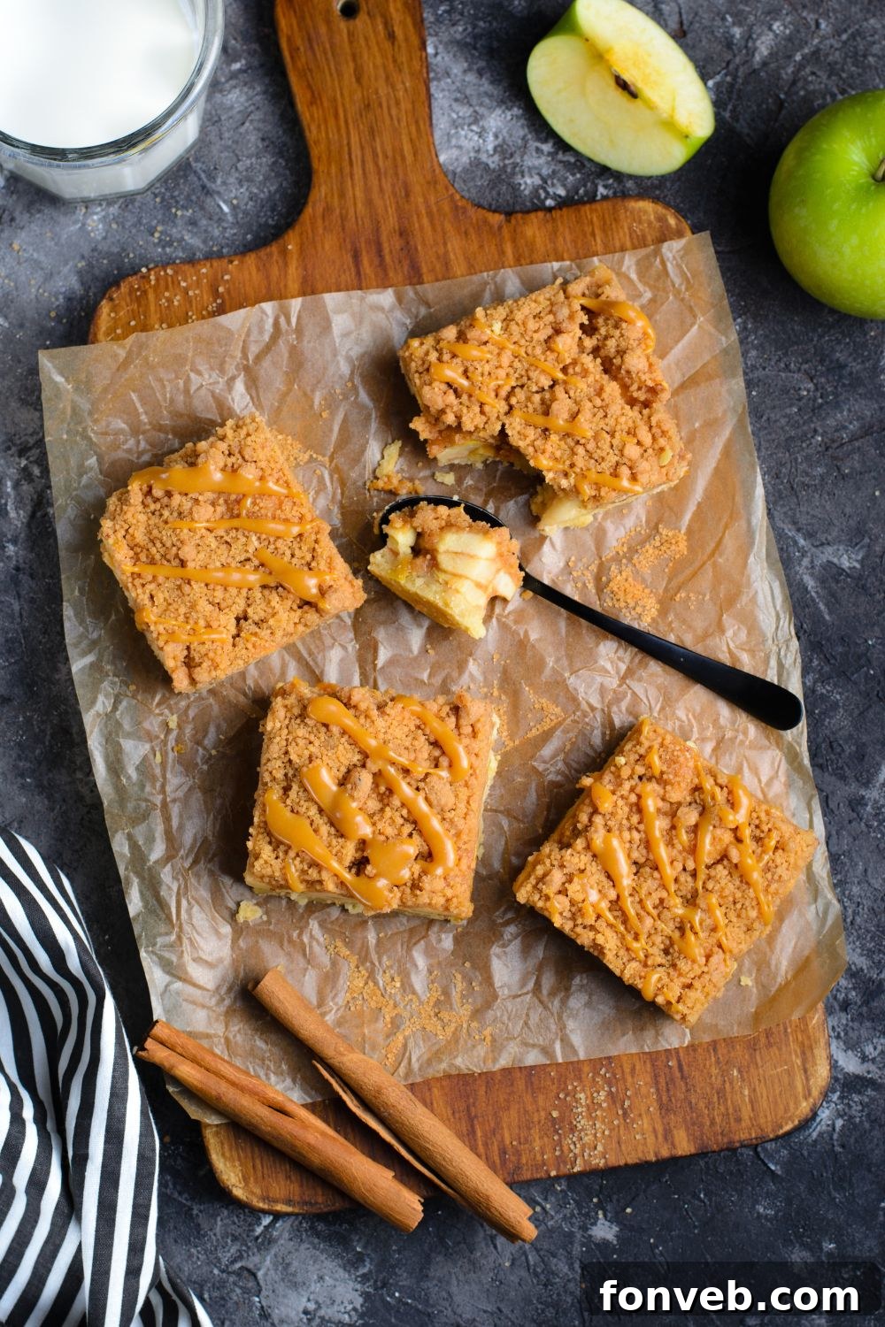 wooden cutting board with slices of apple bars on table with apples around table