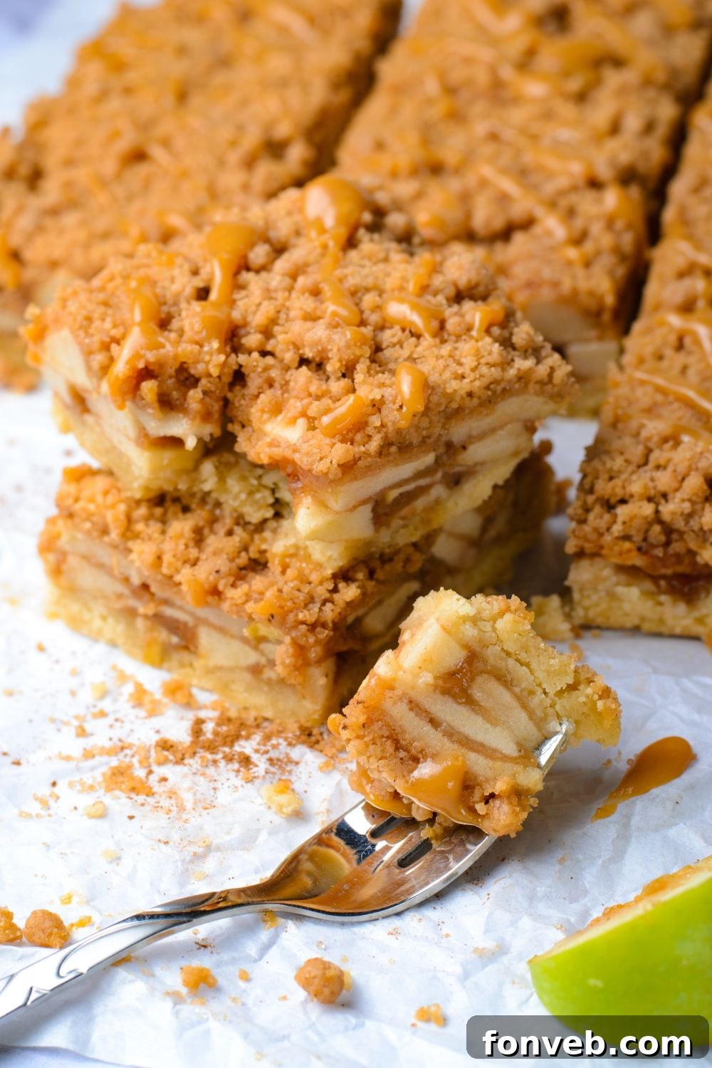Caramel Apple Pie Bars spread out on a table with a bite taken out of the bar on a fork to side on table with a slice of green apple