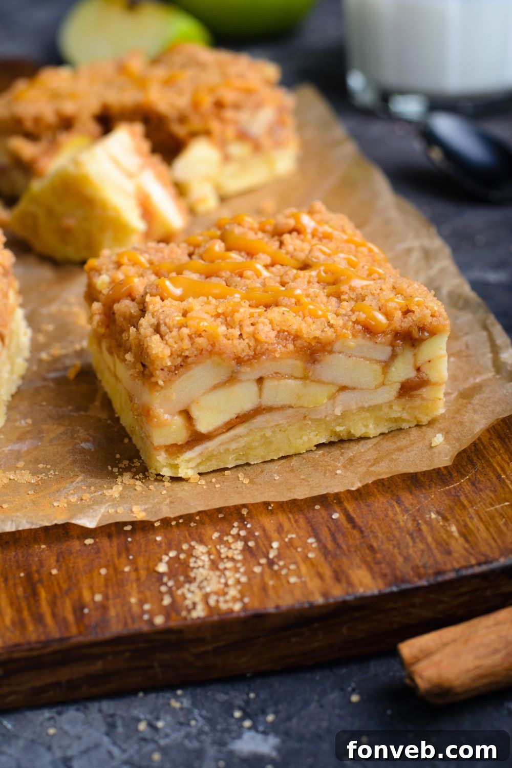 Caramel Apple Pie Bar on wooden cutting board showing the layers of apples with a cinnamon stick in front