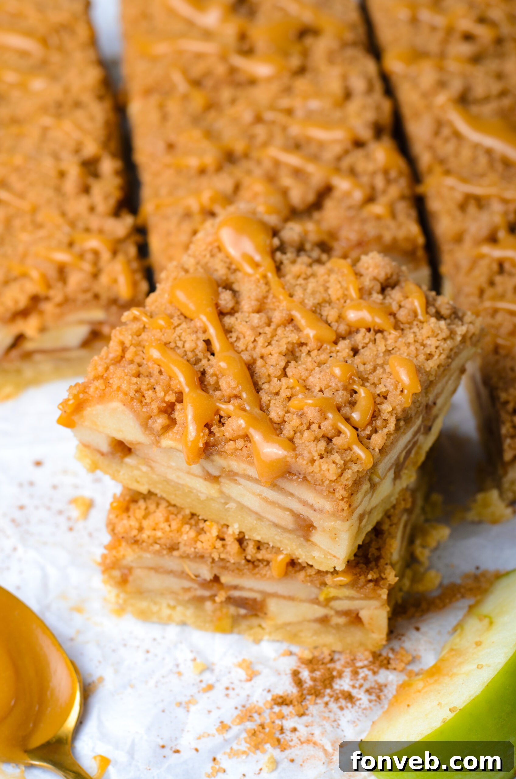 Caramel Apple Pie Bars stacked then placed on parchment paper showing apples in the center of the bars