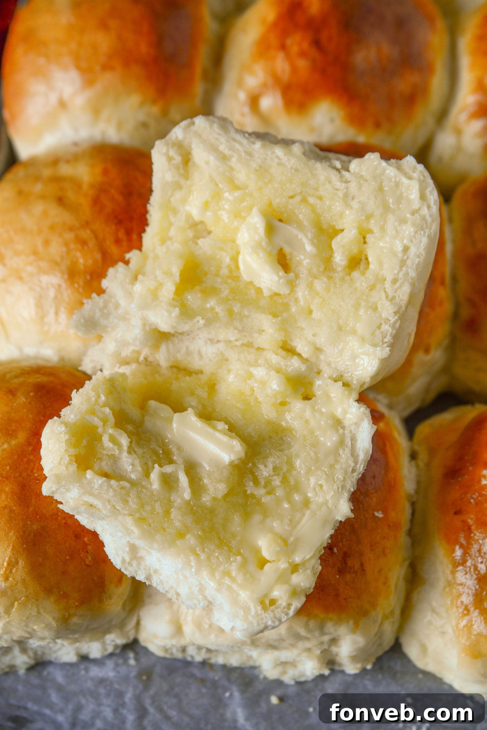 A top-down view of several golden, fluffy dinner rolls on a baking sheet.