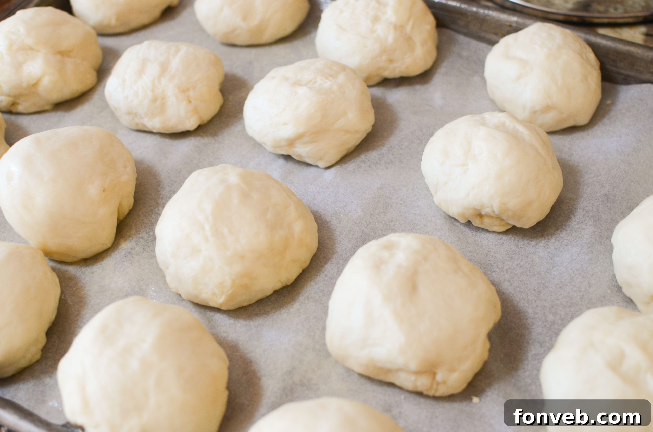 Several soft, golden dinner rolls cooling on a wire rack, with some already buttered.