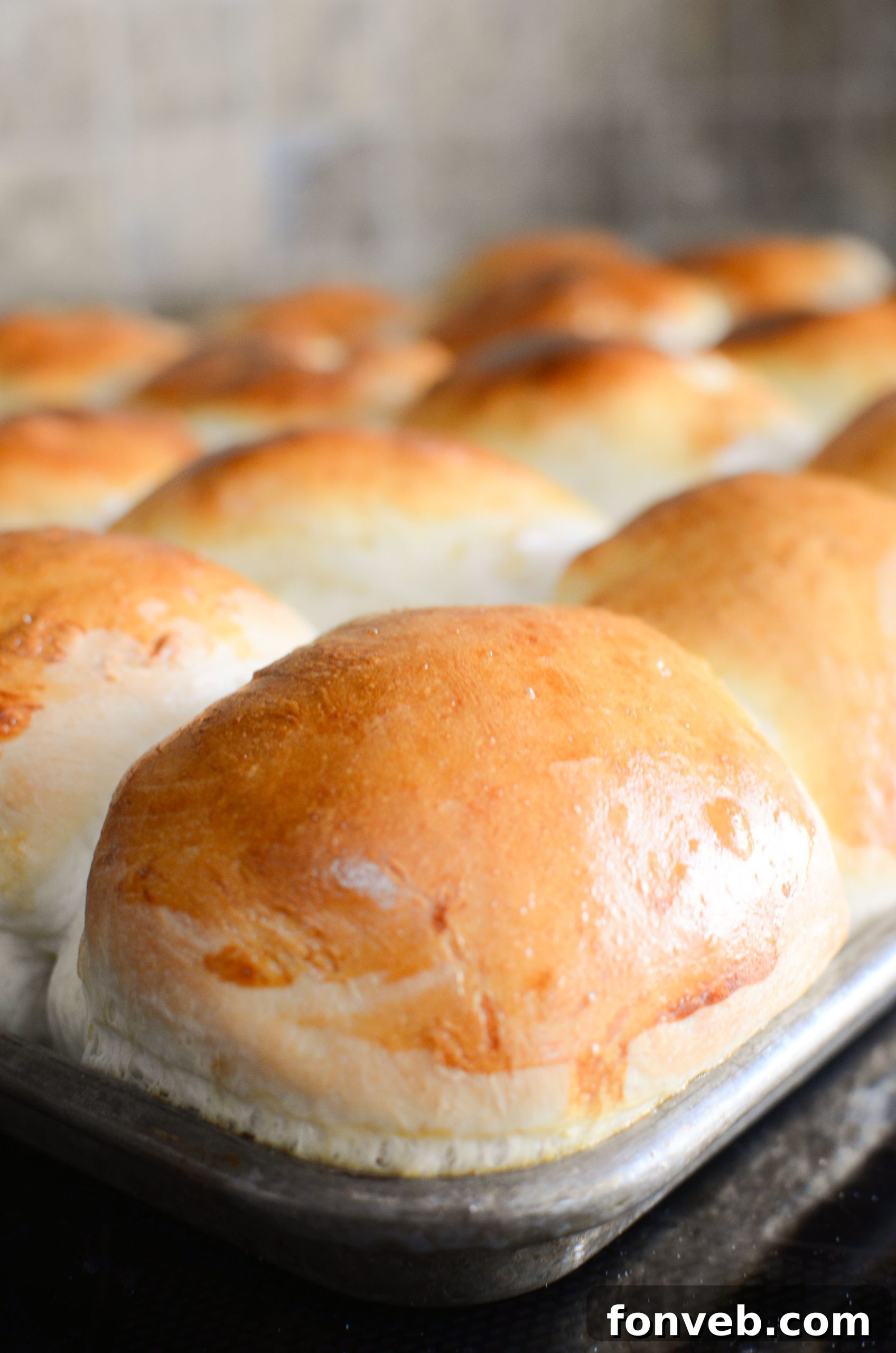 A hand gently tearing apart a warm, freshly baked dinner roll, revealing its soft interior.