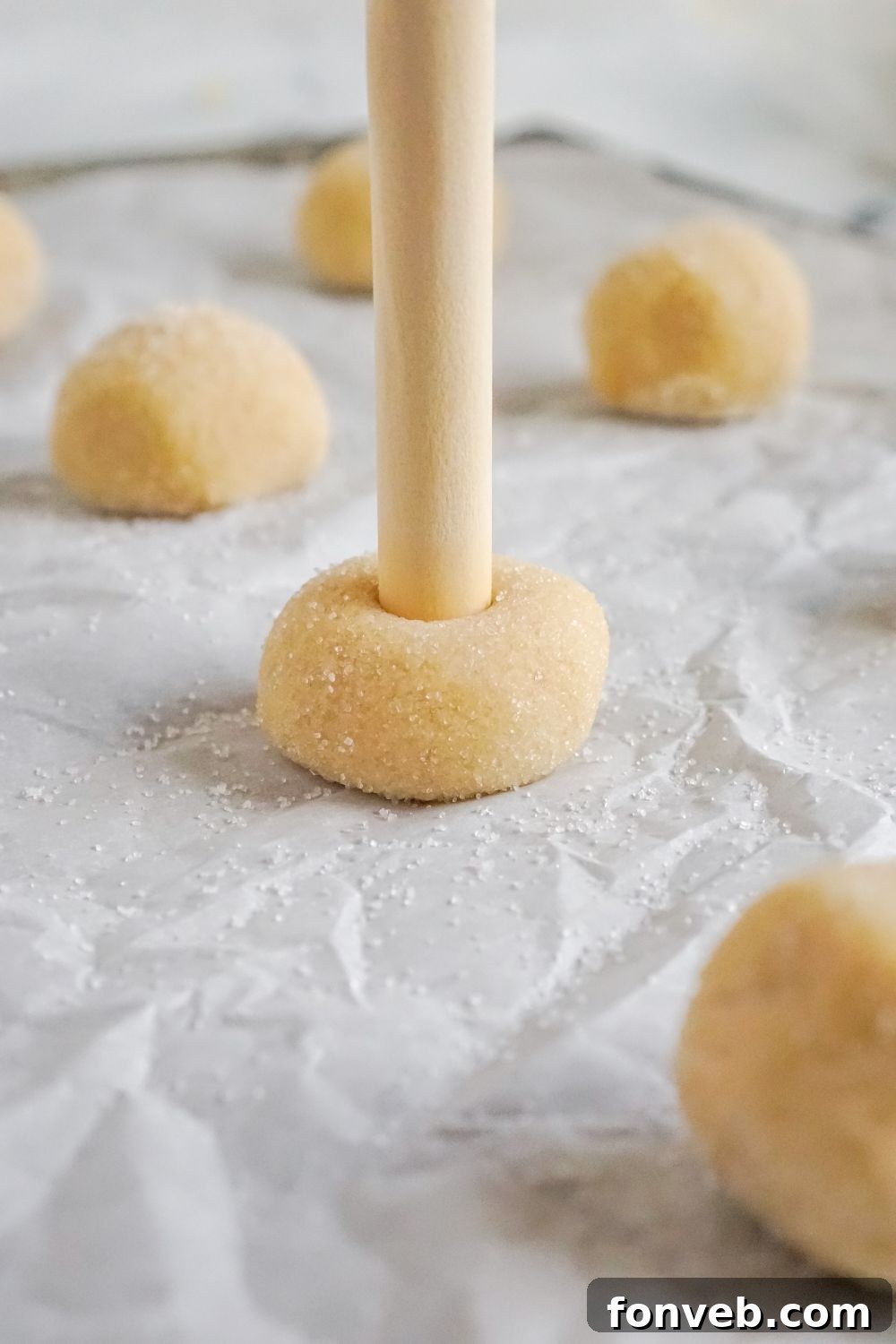 wooden stick poking into the center of thumbprint cookie dough that was rolled into a ball