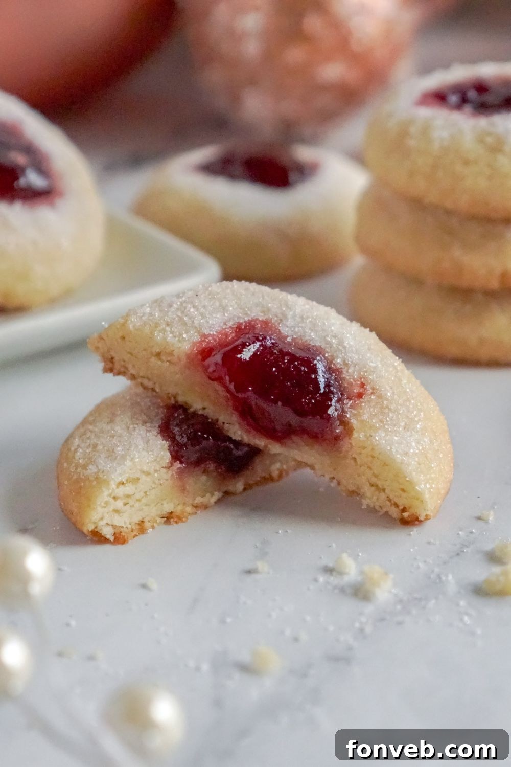 Raspberry Thumbprint Cookie cut in half and placed on table with a stack of cookies behind it on table