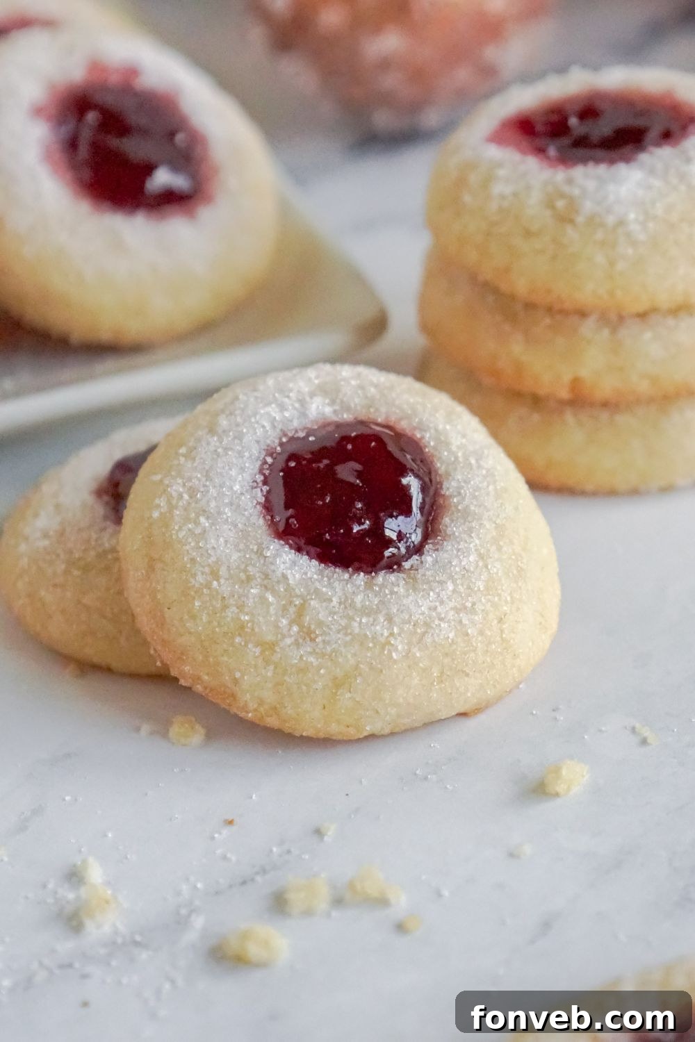 Raspberry Thumbprint Cookies placed around the table and some cookies are in a stack