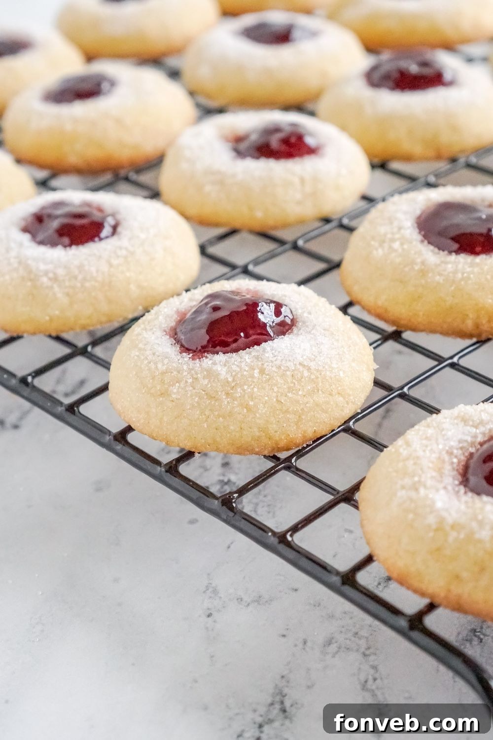 Raspberry Thumbprint Cookies on a cooling rack on a marble counter showing a side of the cookies