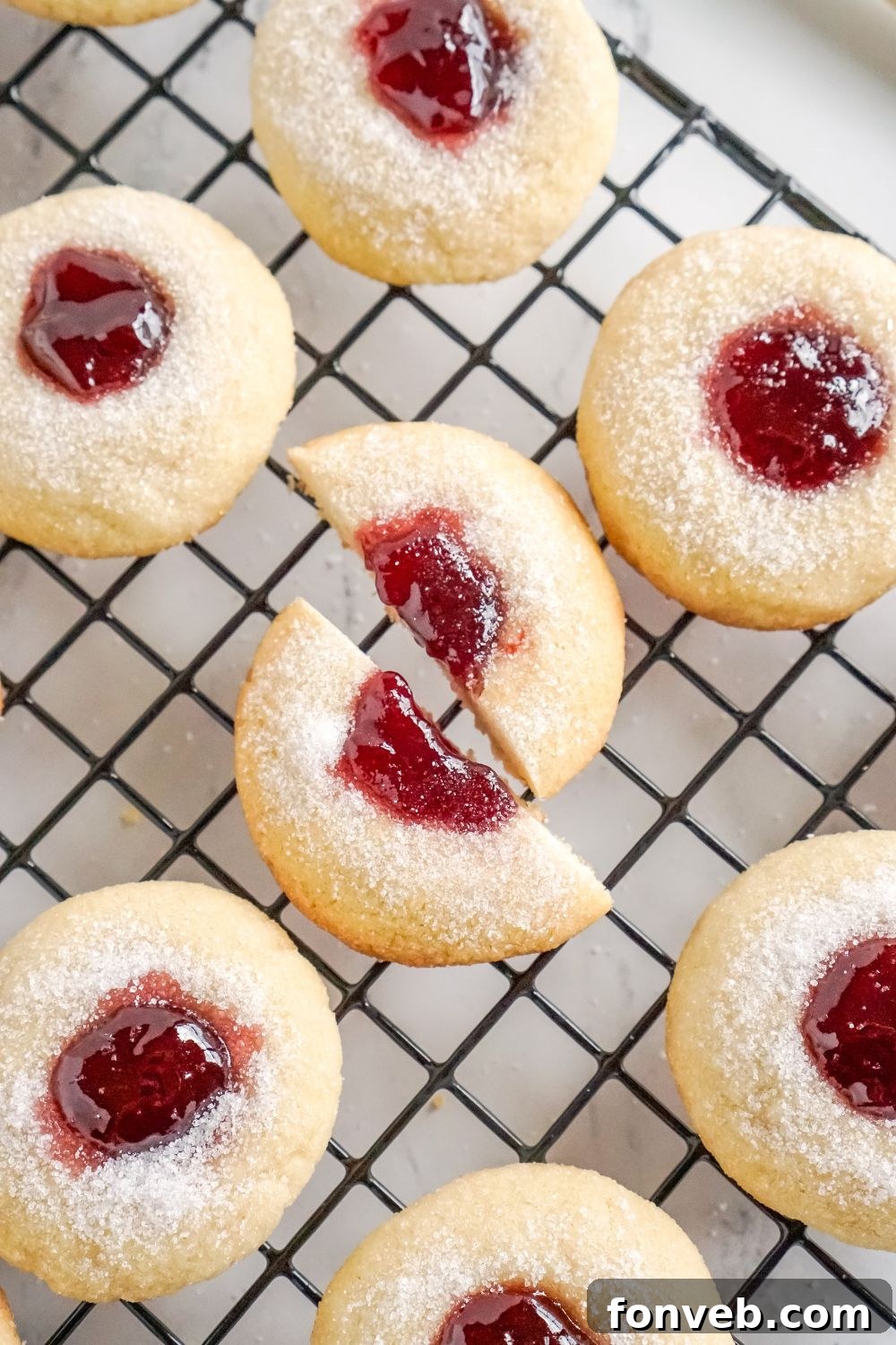 close up look of Raspberry Thumbprint Cookies on cooling rack with one cookie cut in half