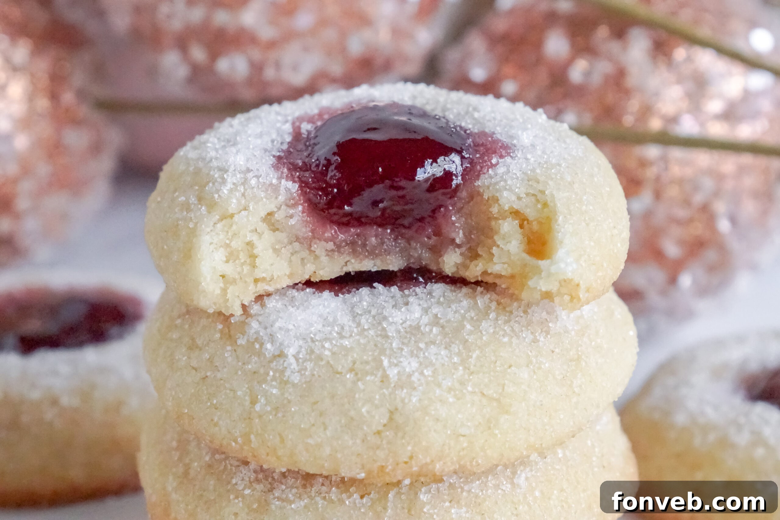 Raspberry Thumbprint Cookies stacked on top of one another with a bite missing from the top one