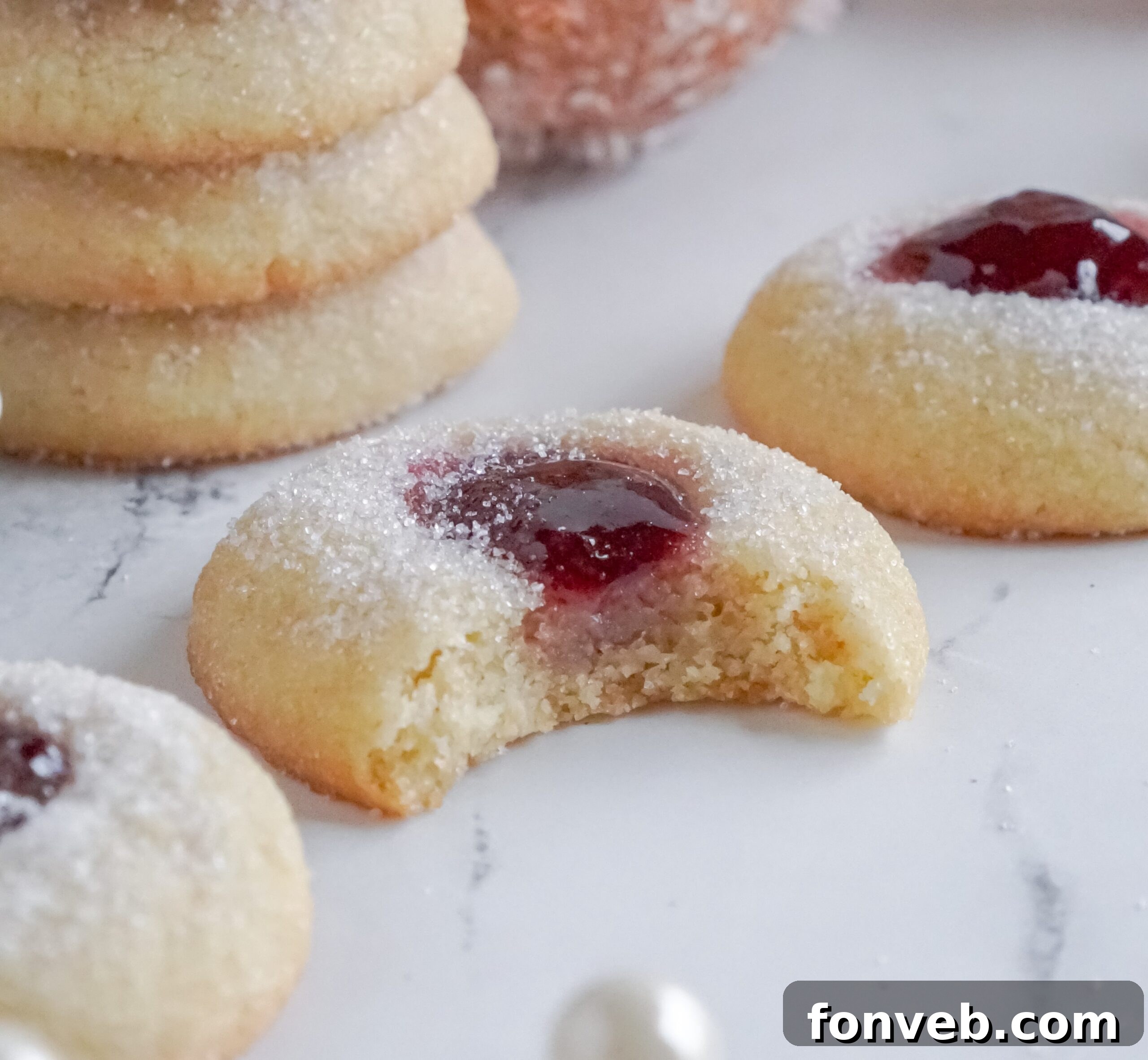 Raspberry Thumbprint Cookie with a bite missing on a marble table with more cookies spread around it