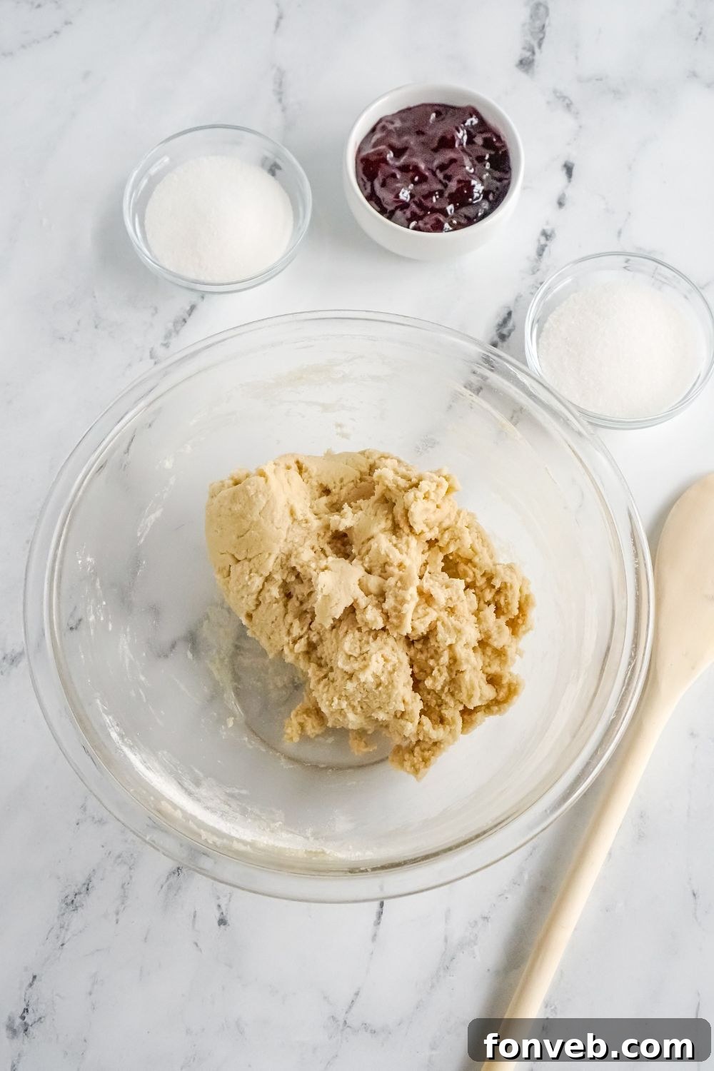 cookie dough in glass bowl on marble counter with other bowls of ingredients to side
