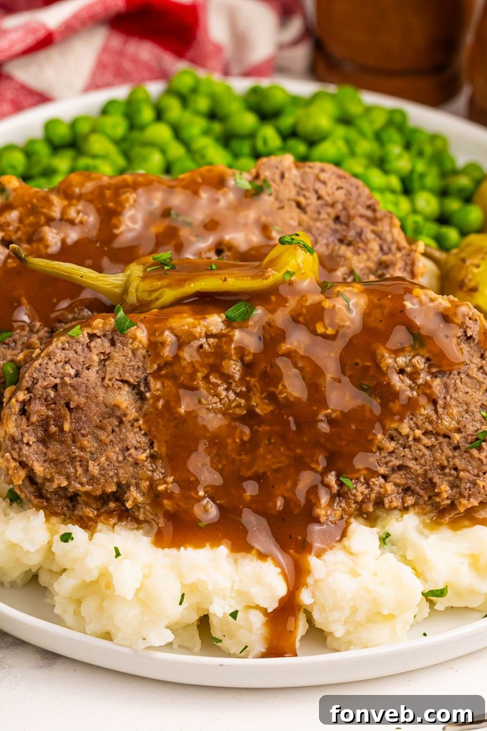 Crockpot Mississippi Meatloaf sliced on top of mashed potatoes and peas on the plate 