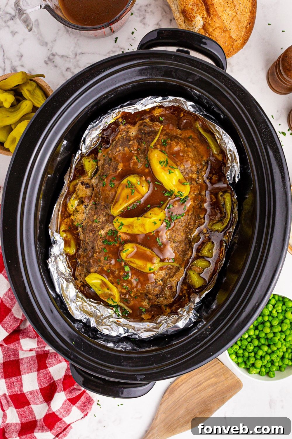black crockpot with Mississippi Meatloaf with gravy and peppers on top and peas and peppers to the side 