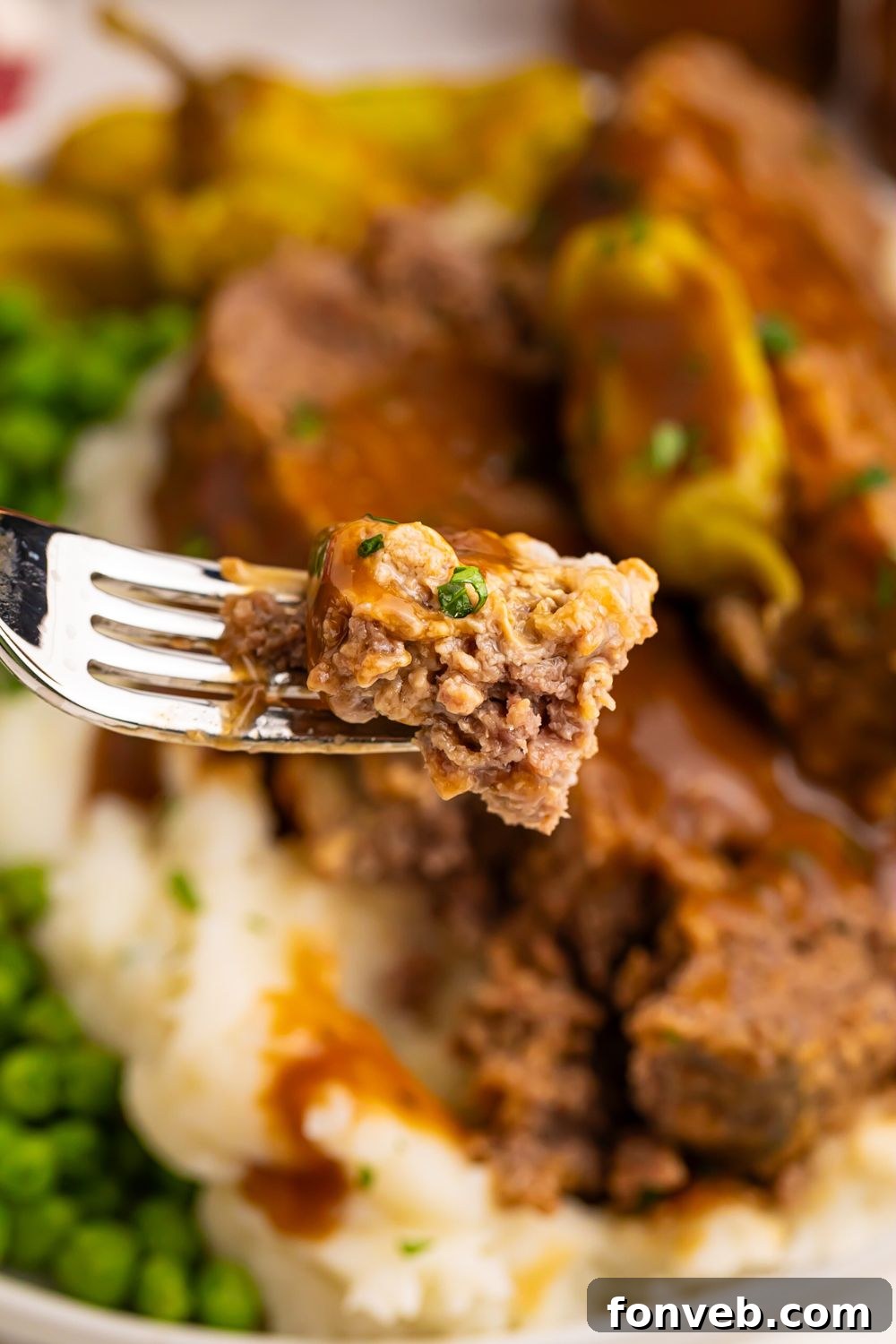 a plate full of Crockpot Mississippi Meatloaf with mashed potatoes and green peas with a fork with a bite of the meatloaf on it 