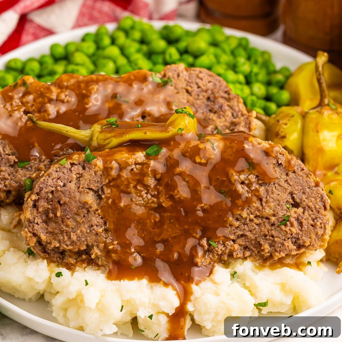 Mashed potatoes topped with Crockpot Mississippi Meatloaf and a side of green peas on a large plate on a wooden table 