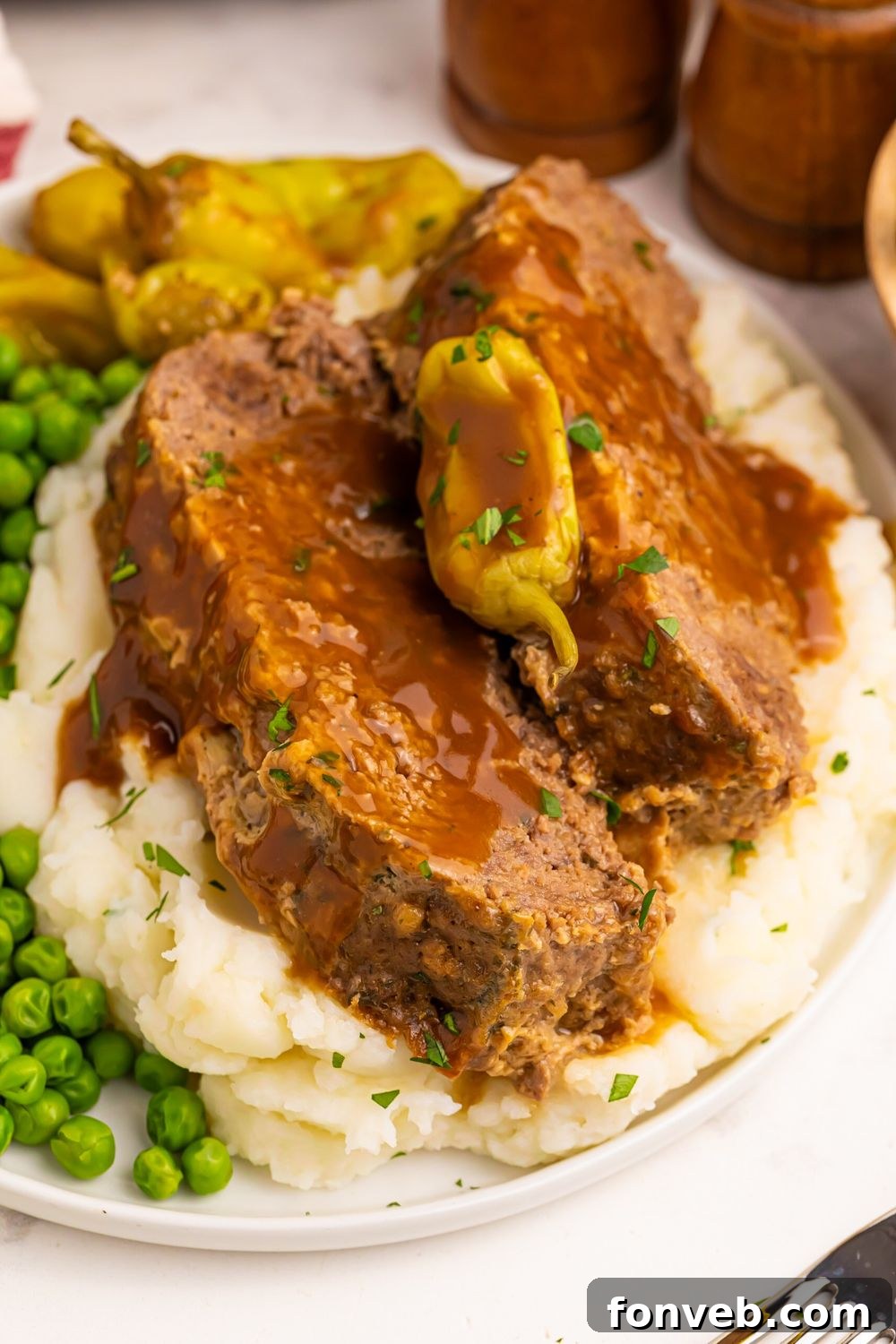 Crockpot Mississippi Meatloaf sliced and placed on mashed potatoes with some peas to side and wooden salt and pepper shakers