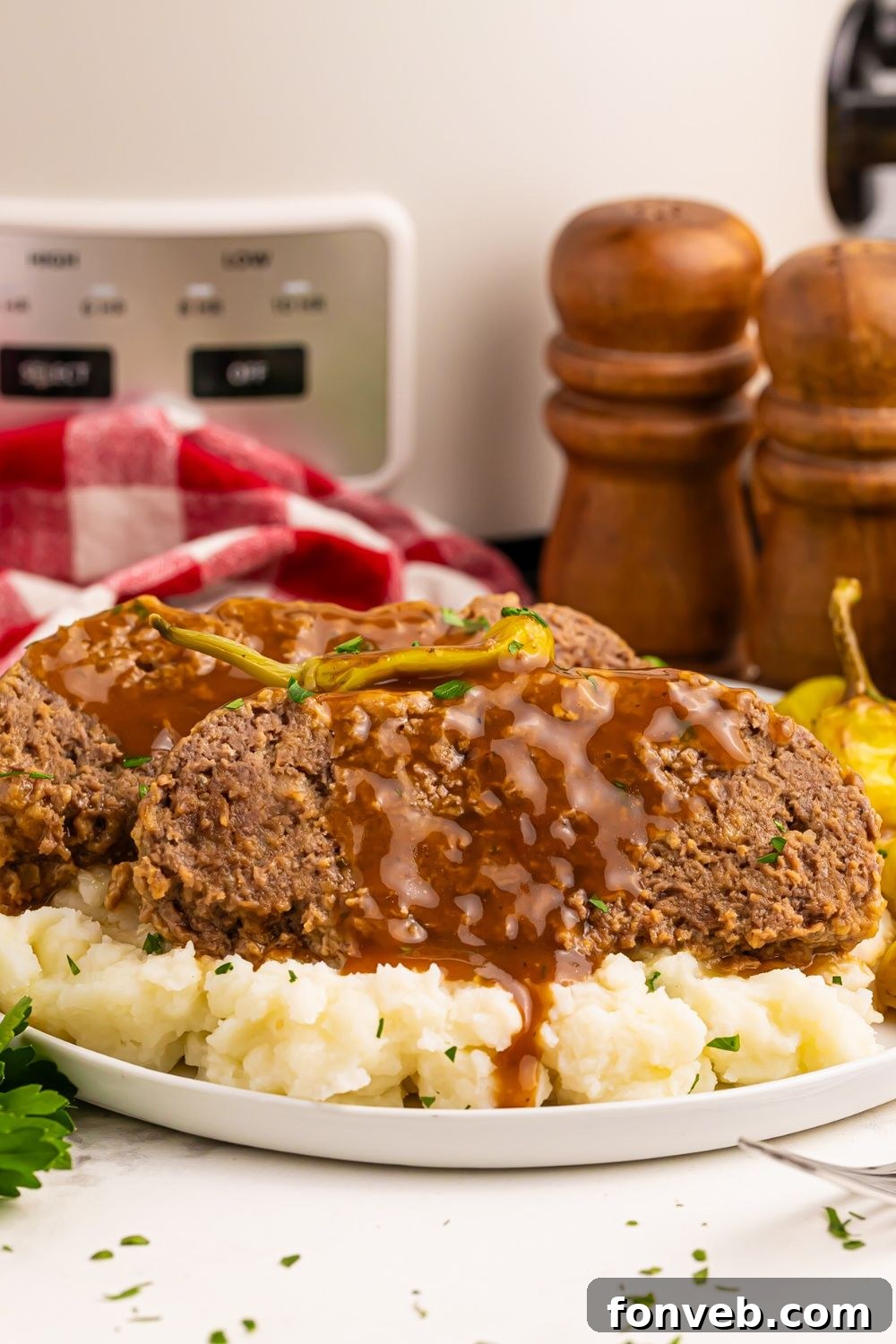 view of table with mashed potatoes  with slices of meatloaf on a plate with a red checkered towel with slow cooker in the background 