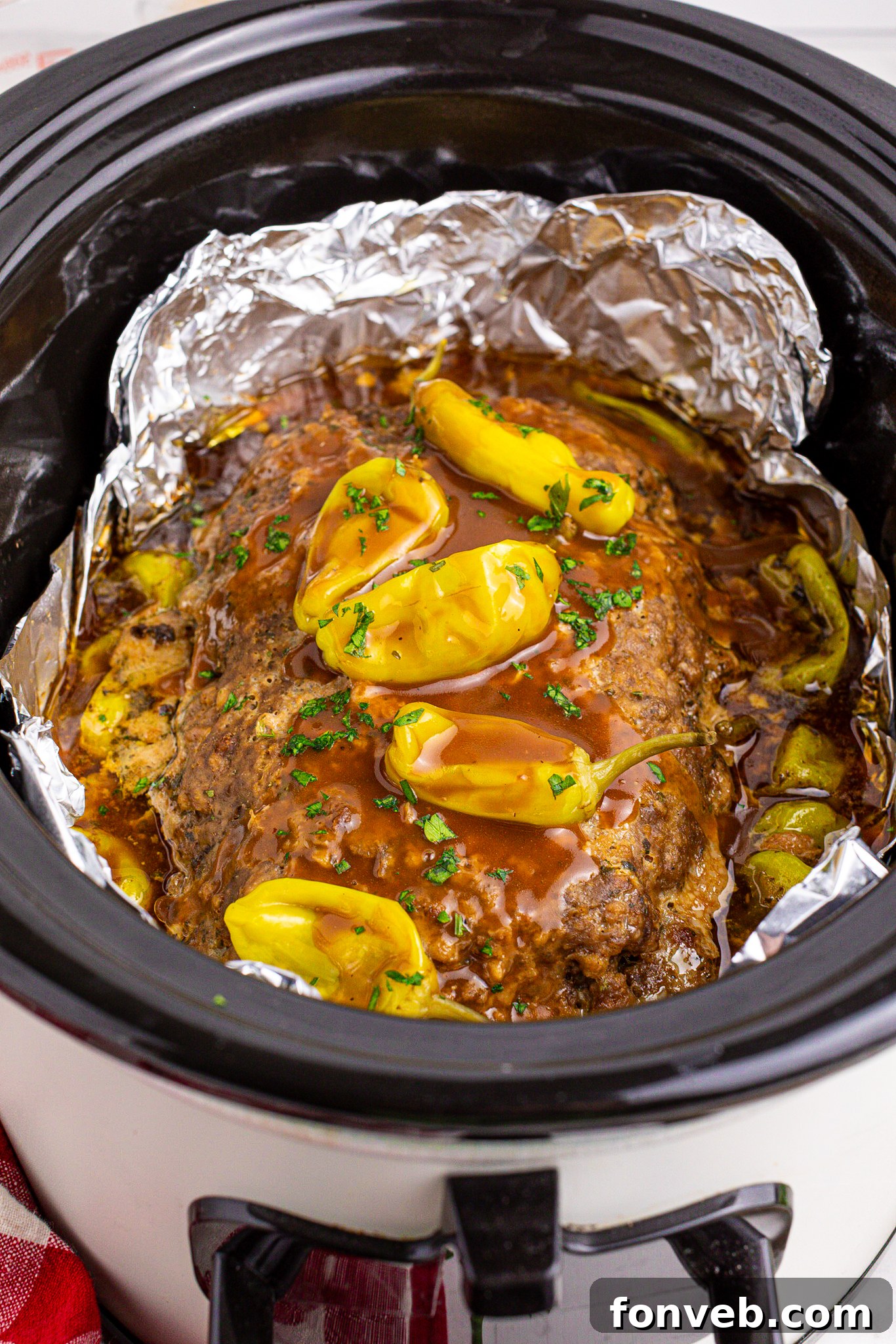 Crockpot Mississippi Meatloaf in a black slow cooker lined with foil topped with gravy and peppers 
