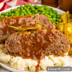 Mashed potatoes topped with Crockpot Mississippi Meatloaf and a side of green peas on a large plate on a wooden table