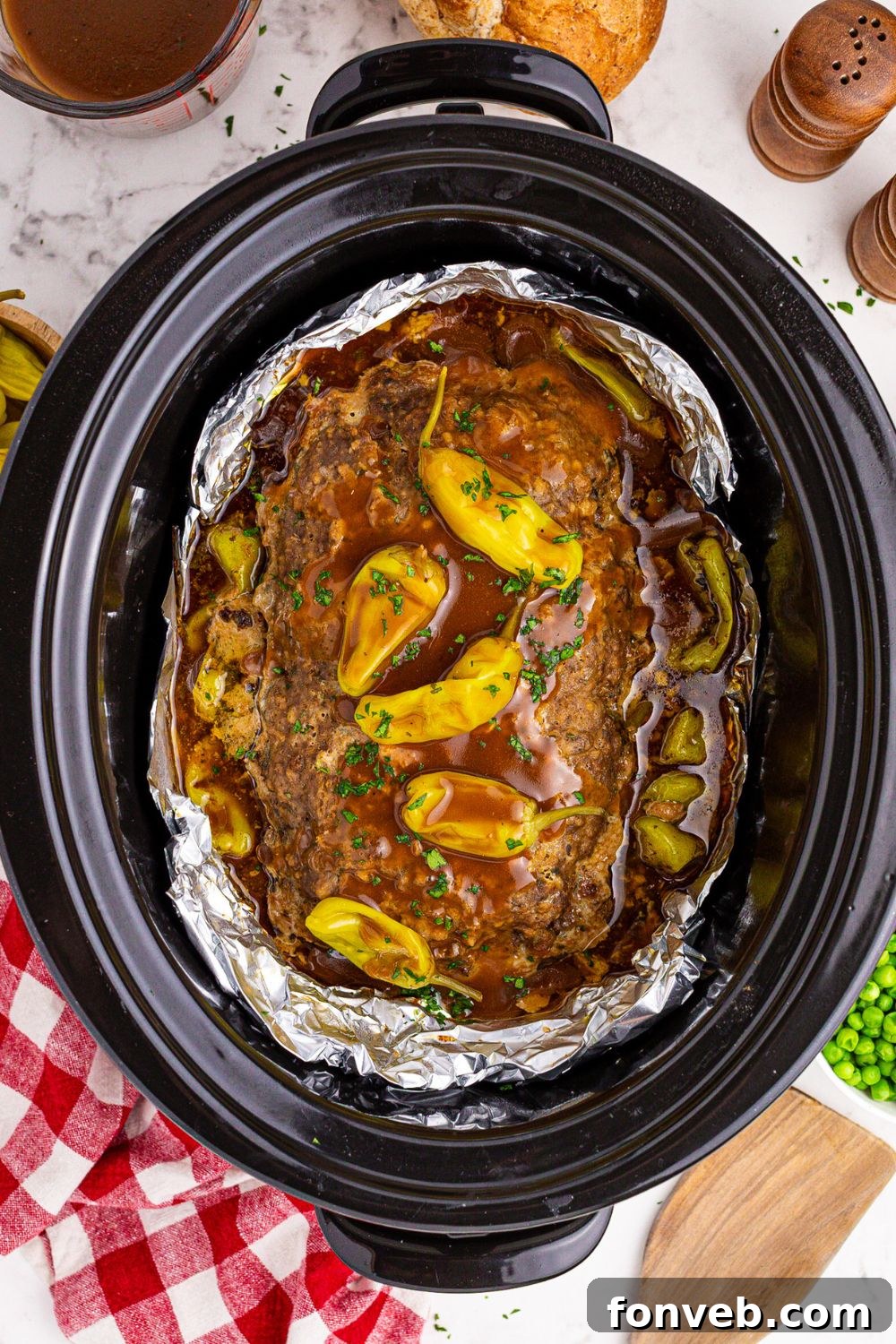 Crockpot Mississippi Meatloaf in a crockpot with peppers and gravy poured over the top of it on the table 