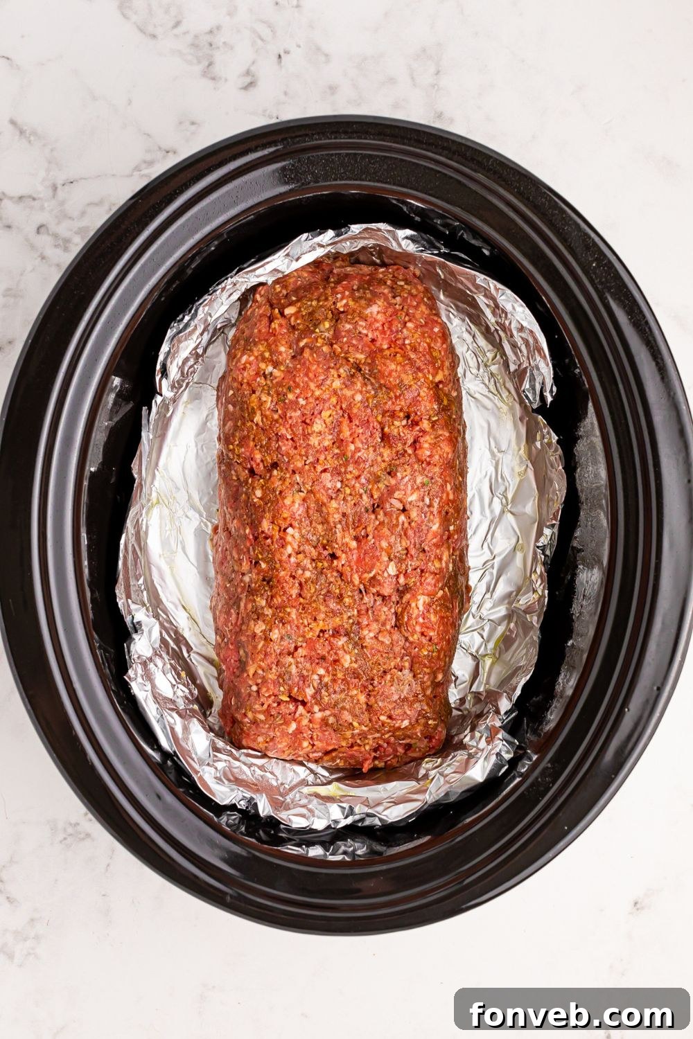 black crockpot on table with foil and a meatloaf log in center of crockpot 