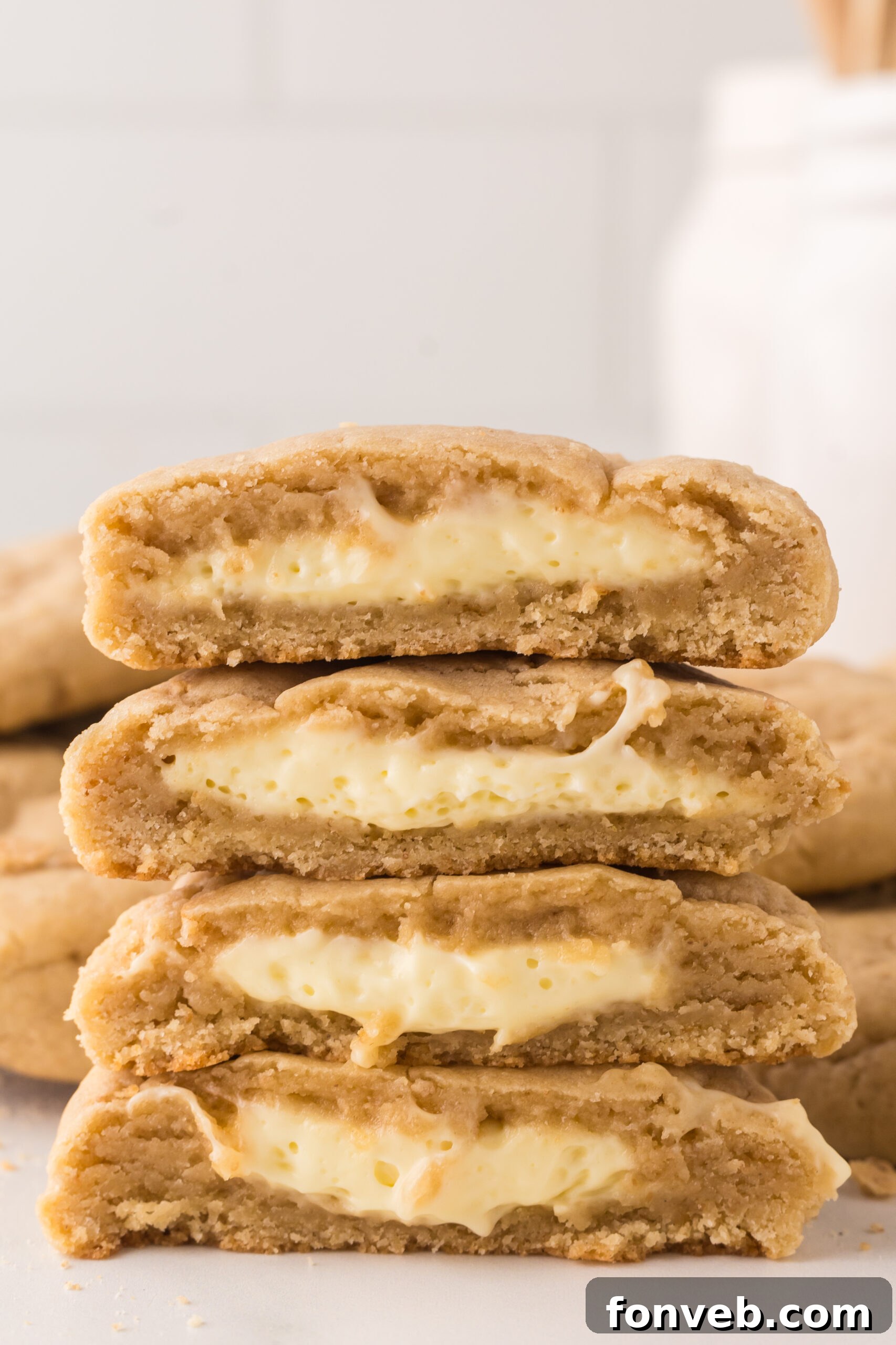 New York cheesecake cookies stacked on top of one another with one cut in half with a glass of milk behind it
