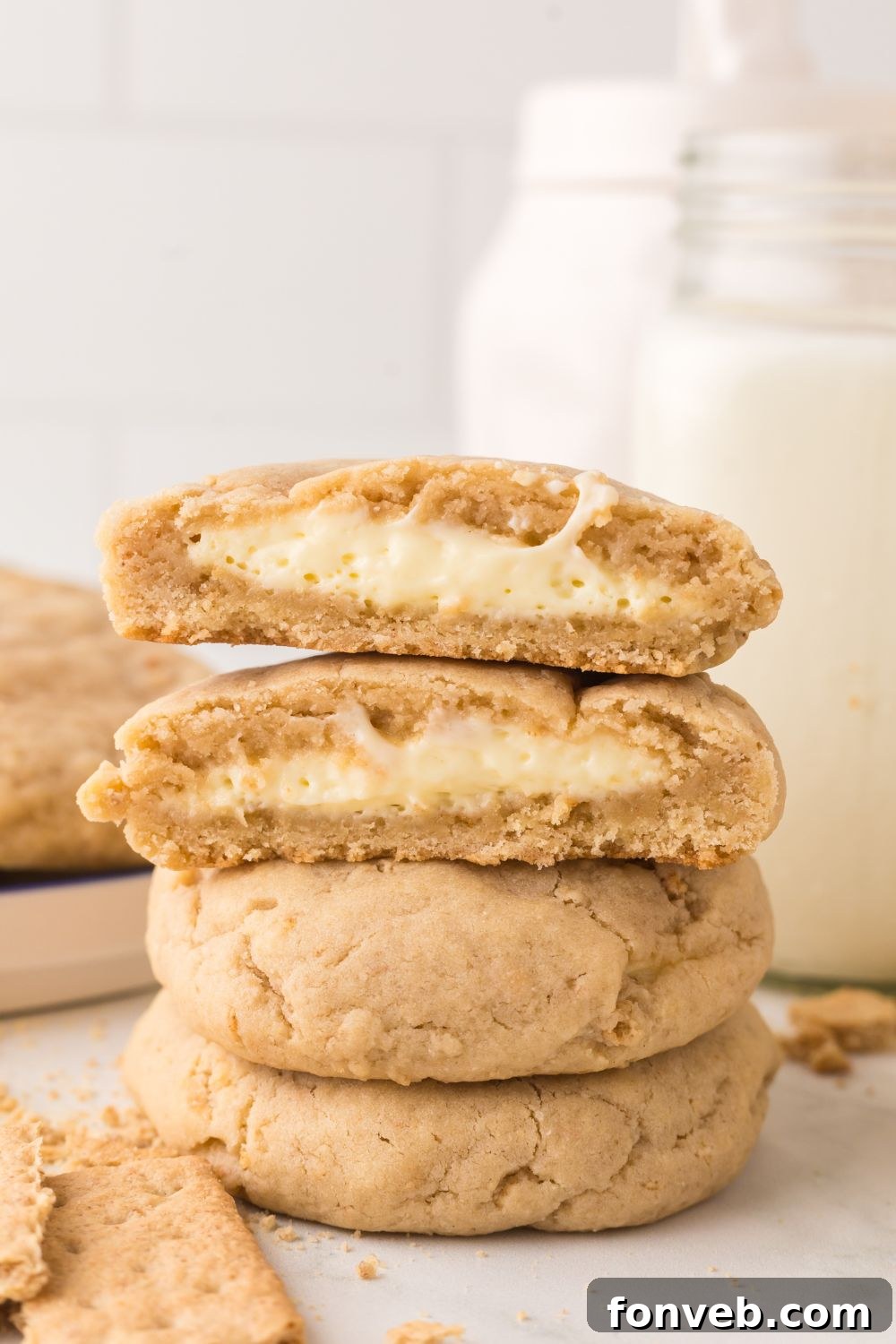 New York cheesecake cookies stacked on top of one another with one cut in half with a glass of milk behind it