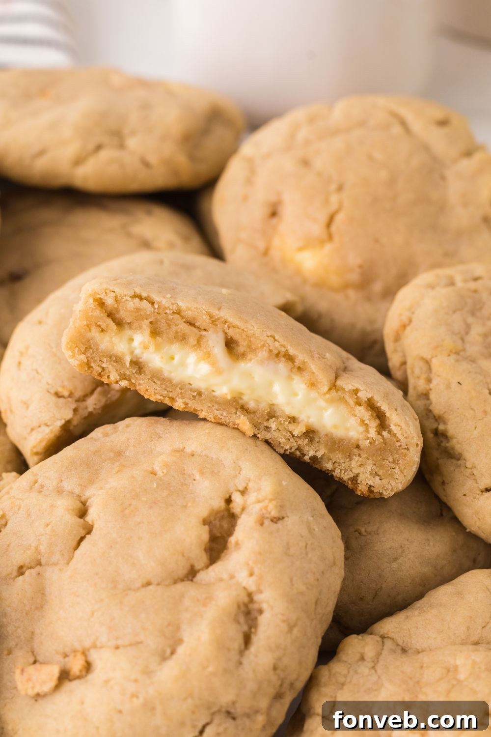 New York cheesecake cookies stacked on table with one cut in half to show the creamy filling in the cookies
