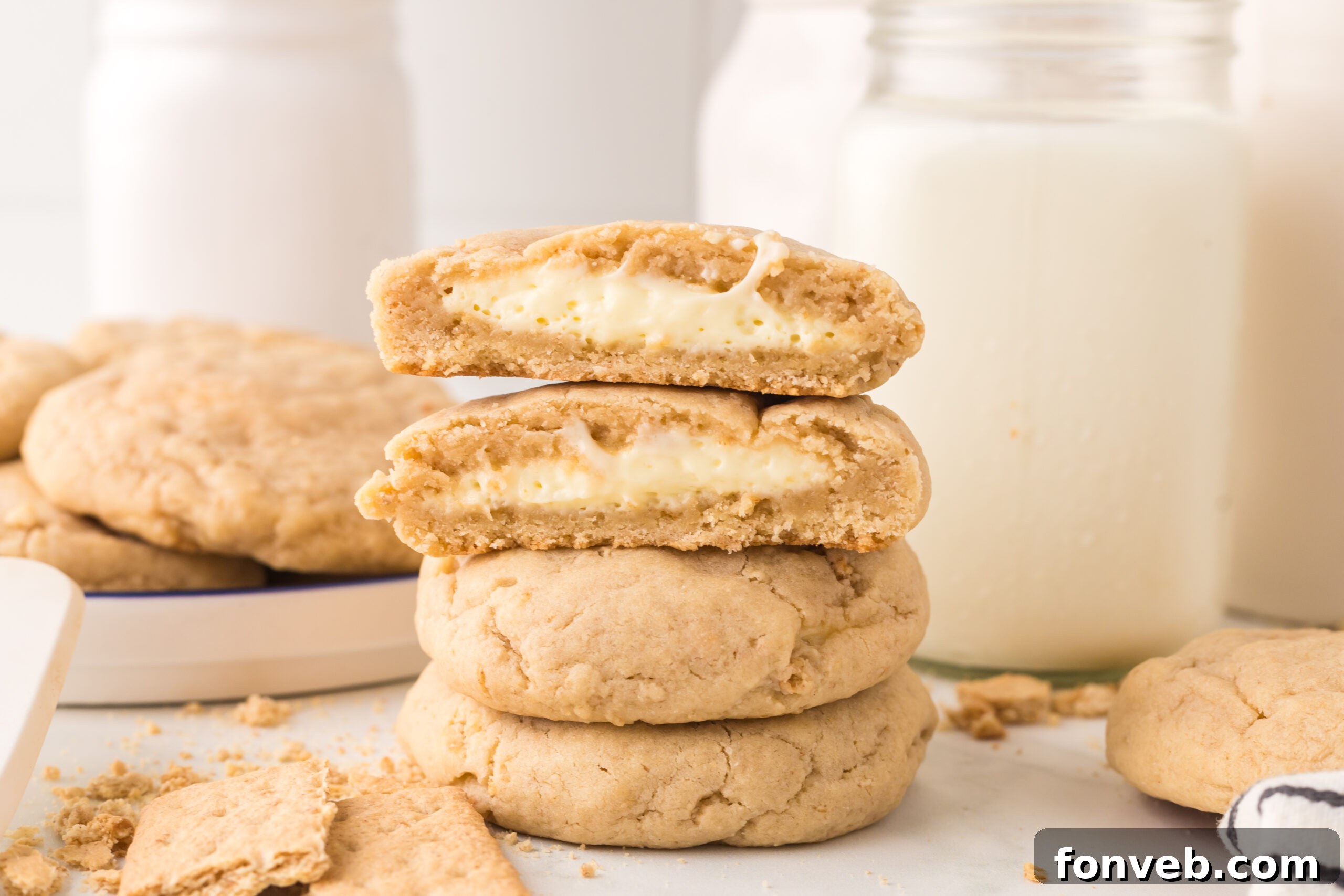 New York cheesecake cookies stacked on top of one another with one cut in half with a glass of milk behind it