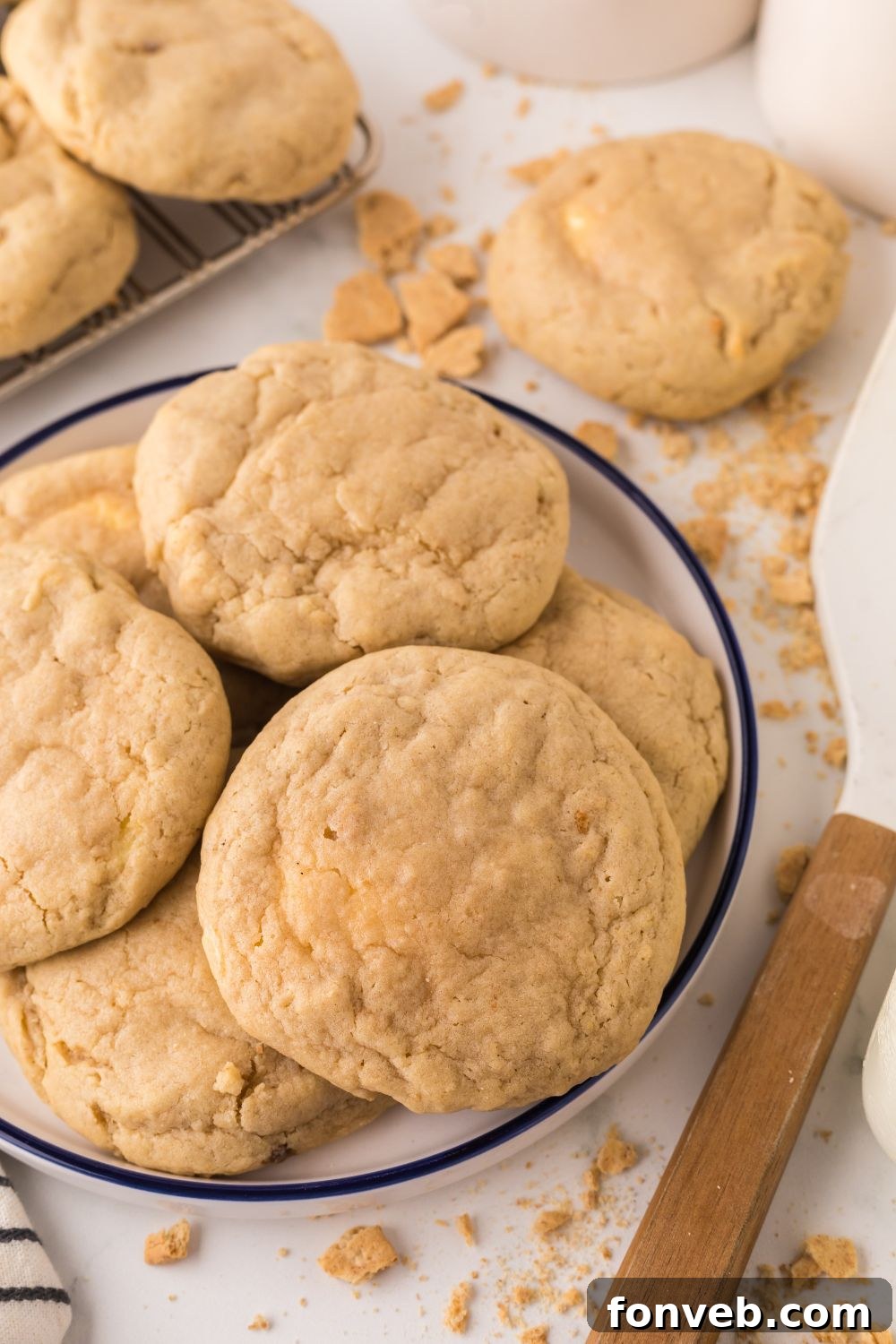 New York cheesecake cookies on a white tray, with more cookies around the table with graham cracker crumbs around the table