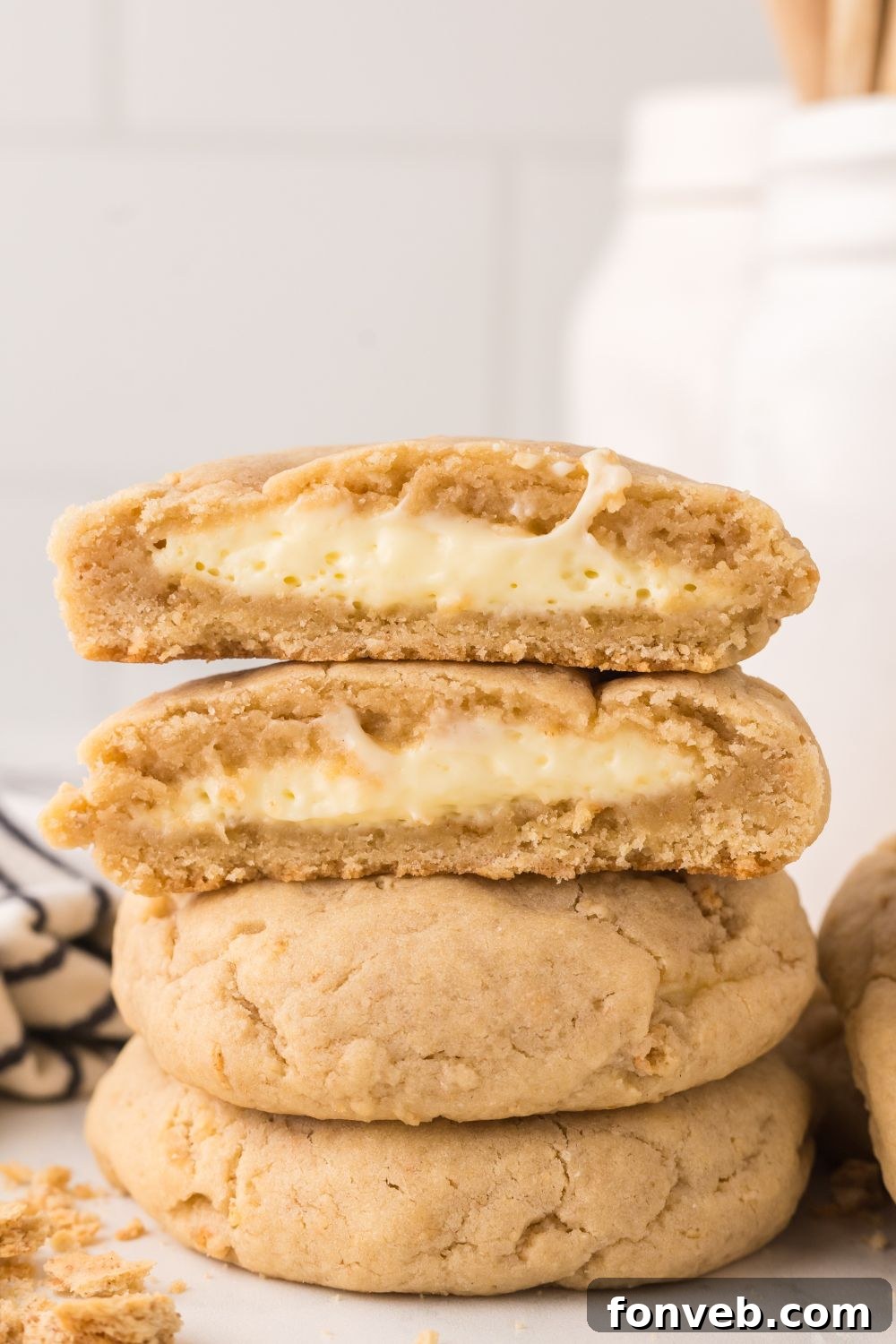 New York cheesecake cookies stacked on marble counter with the top cookie cut in half to show it is a stuffed cream cheese cookie