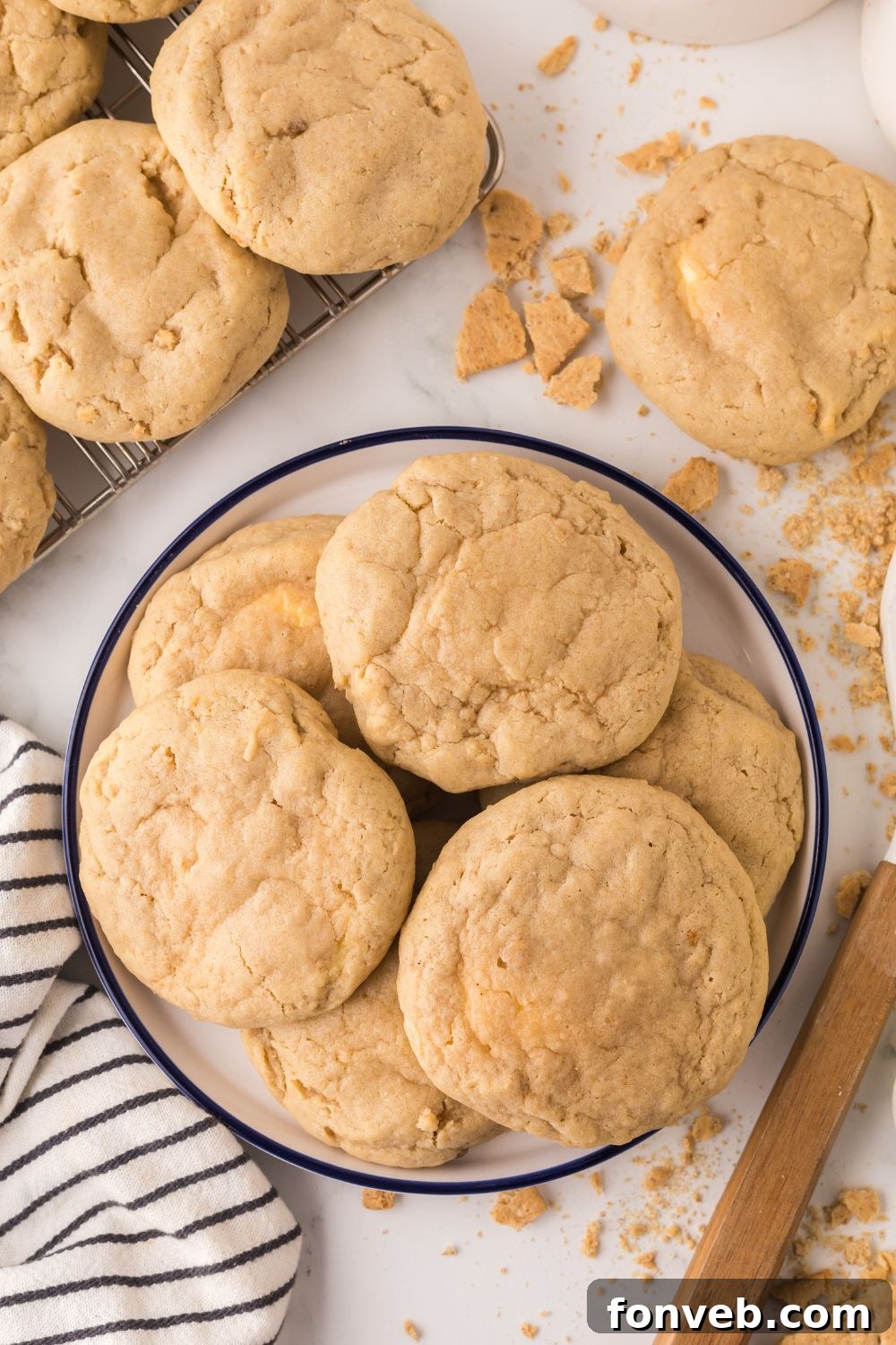 New York cheesecake cookies in a bowl on table with more cookies stacked to side, with graham crackers, towel, and other items around the table