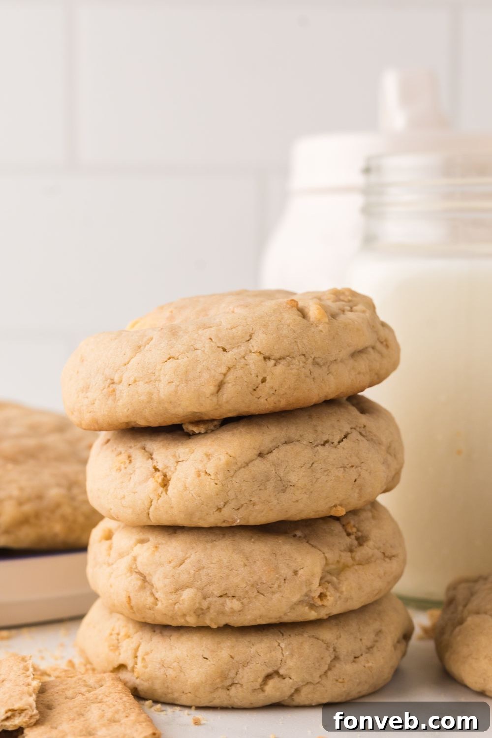 stack of thick cheesecake stuffed cookies on table with a glass of milk behind it and a cutting board with a stack of cookies