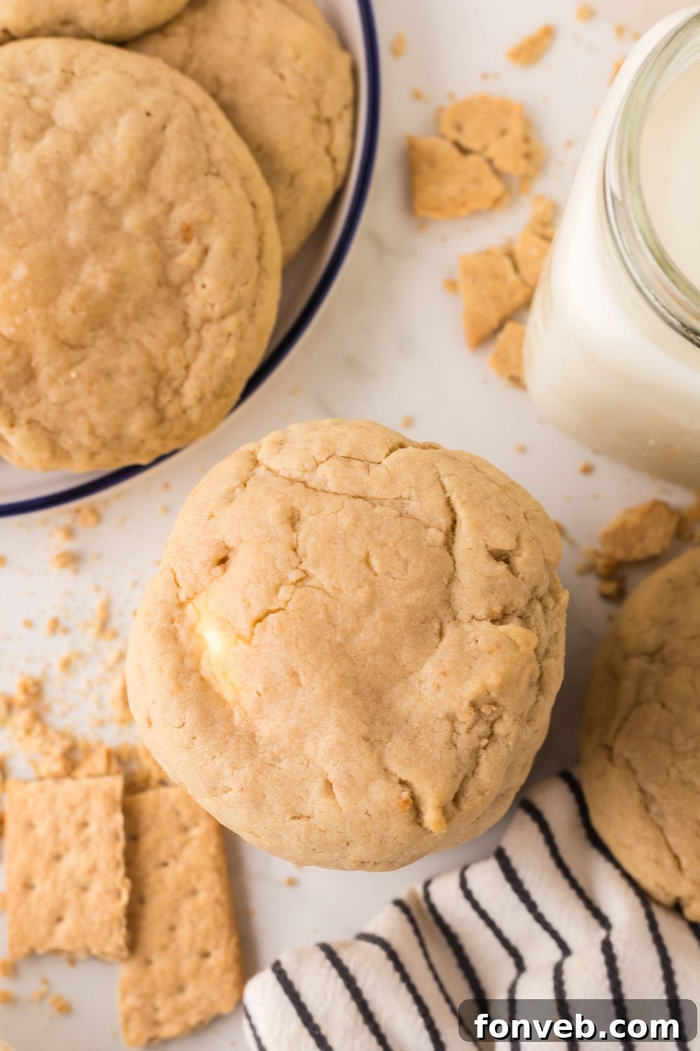 New York Cheesecake Stuffed Cookies stacked on top of one another on white table with a plate with more to side and graham crackers to side
